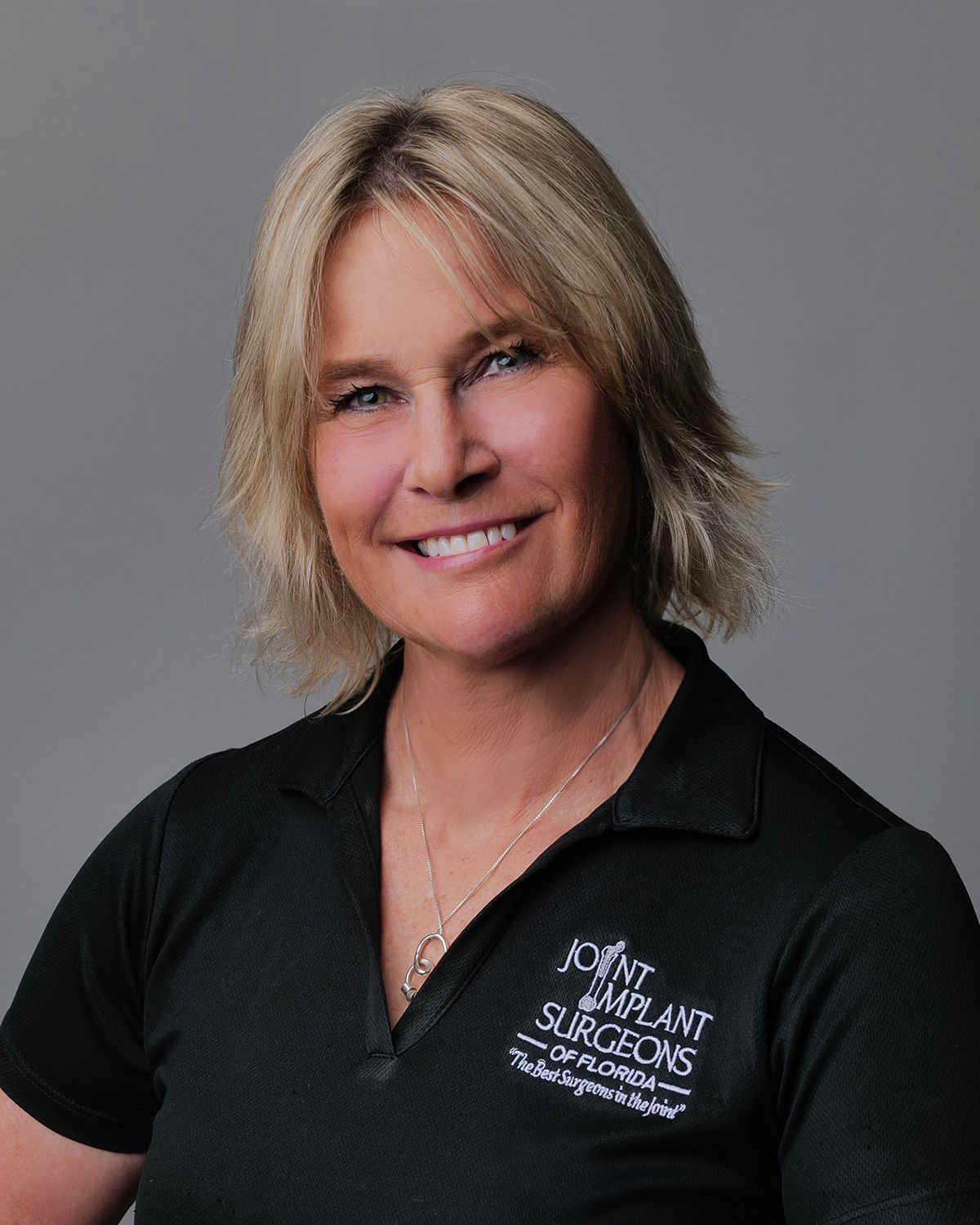 Smiling man in a blue suit and patterned tie, set against a blurred medical office background.