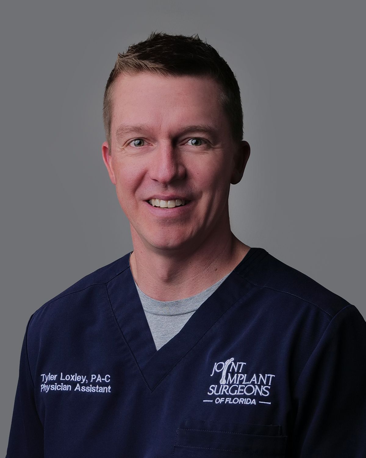 Man in a blue suit smiles, likely a healthcare professional, in a blurred medical setting.