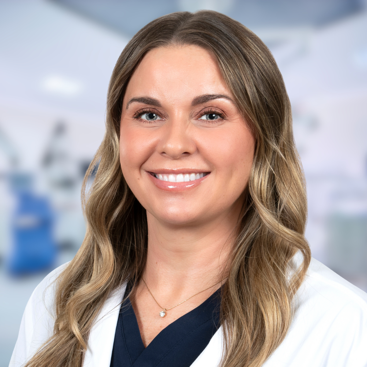 Woman with long, wavy blonde hair, smiling slightly, in a professional setting.