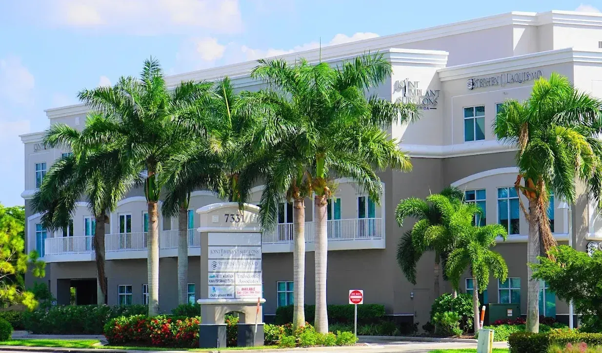 Office building with palm trees in front under a blue sky.