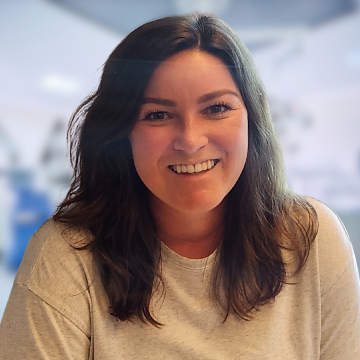 Smiling woman with auburn hair in a black shirt, possibly a doctor, in a medical setting.
