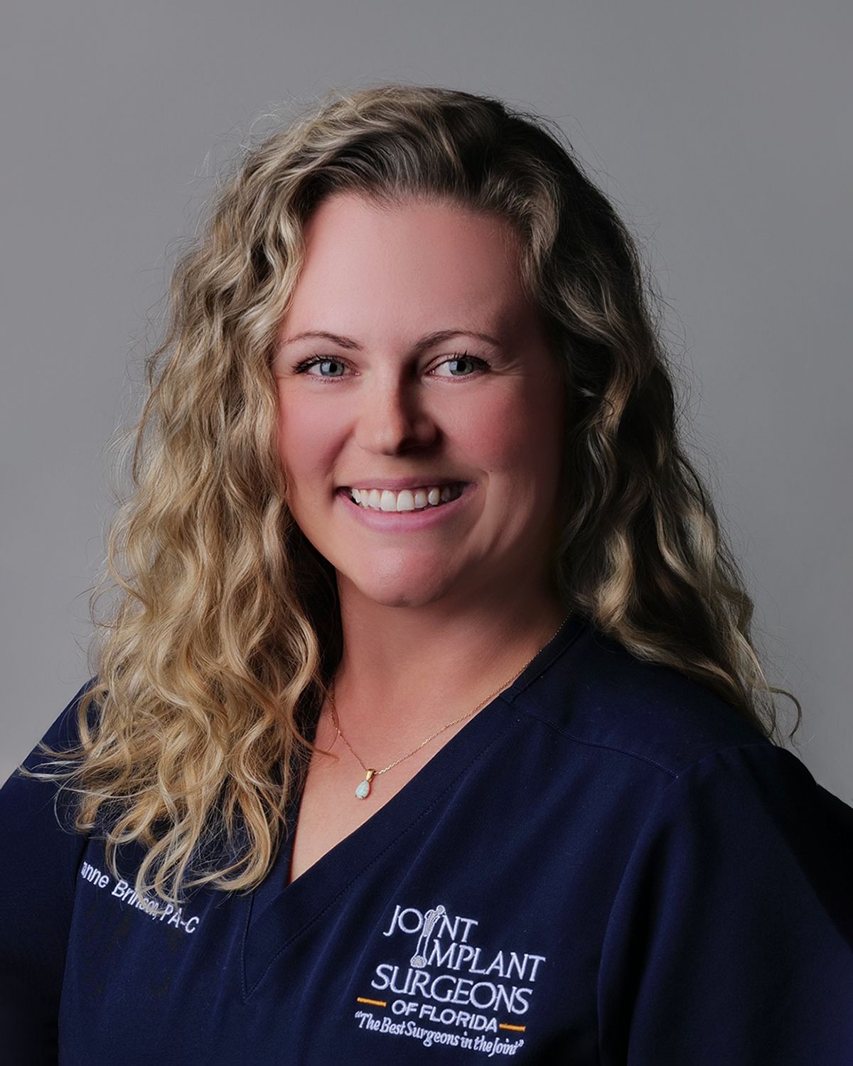 Blonde woman in white coat smiles; medical setting blurred in background.