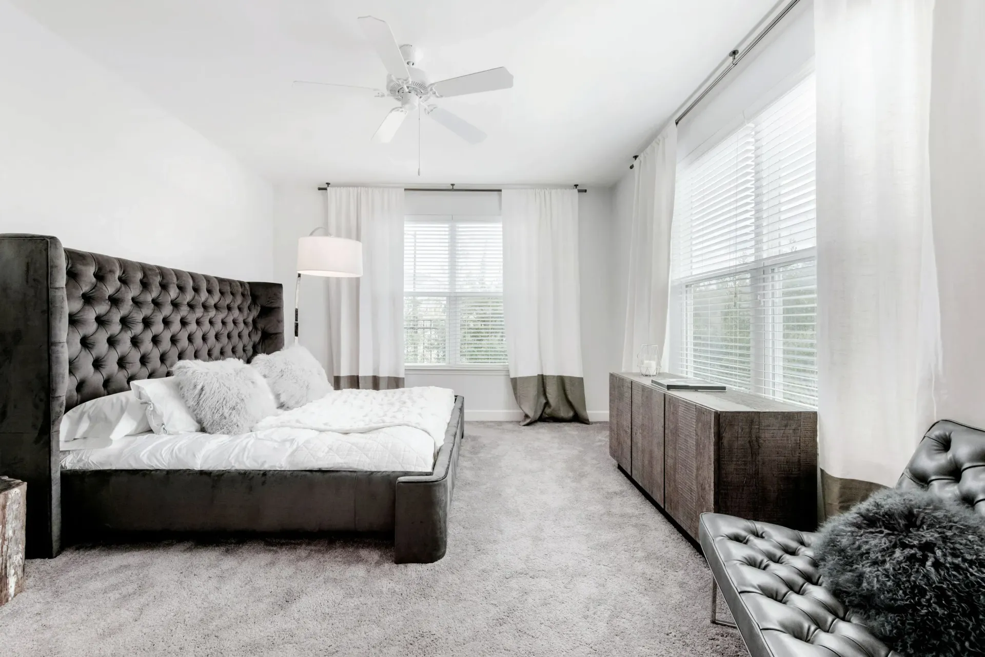 Bedroom in a modern apartment featuring a tufted headboard, white bedding, and large windows.