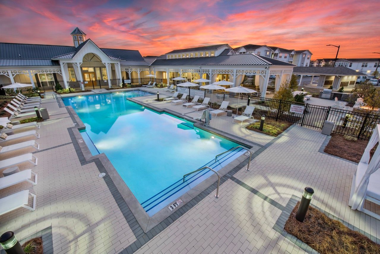 Outdoor resort-style pool area with lounge chairs and a clubhouse at sunset.
