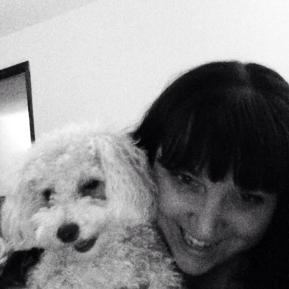 Woman smiling with a small, fluffy white dog, possibly a poodle mix, close-up in black and white.