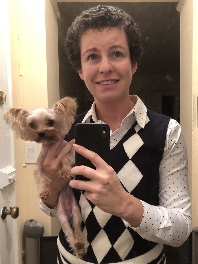 Woman holding a small dog, taking a selfie in a mirror. They both have neutral expressions.