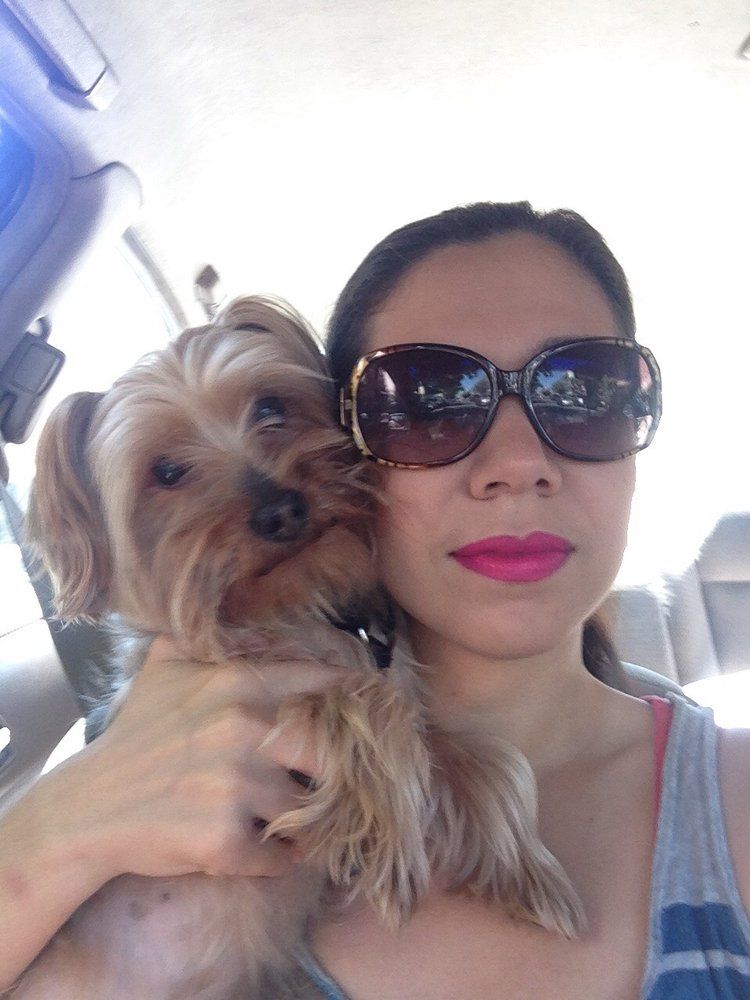 Woman in sunglasses holding small dog in a car.