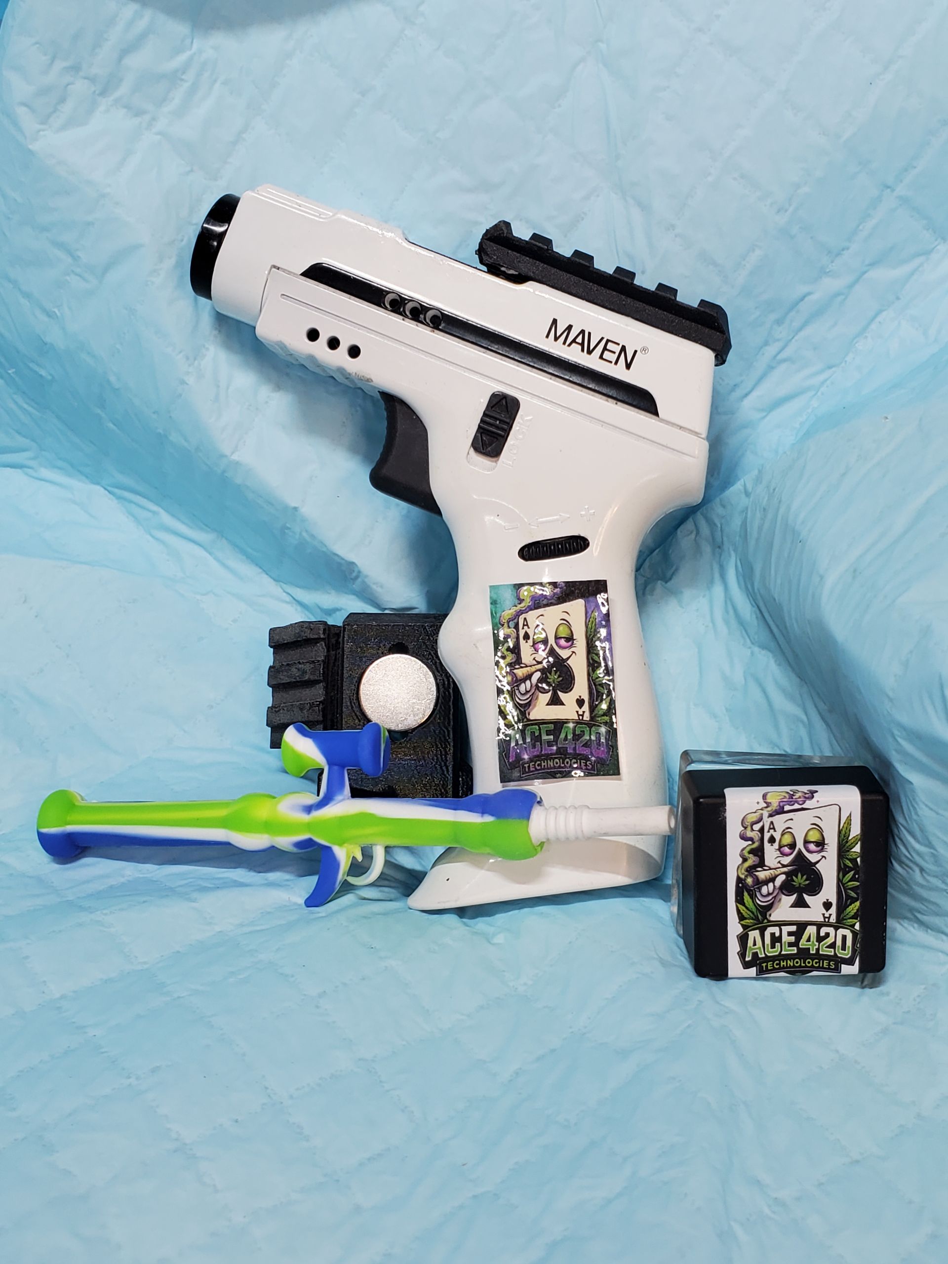White toy gun with green-and-blue attachments and two card packs on a blue quilted background