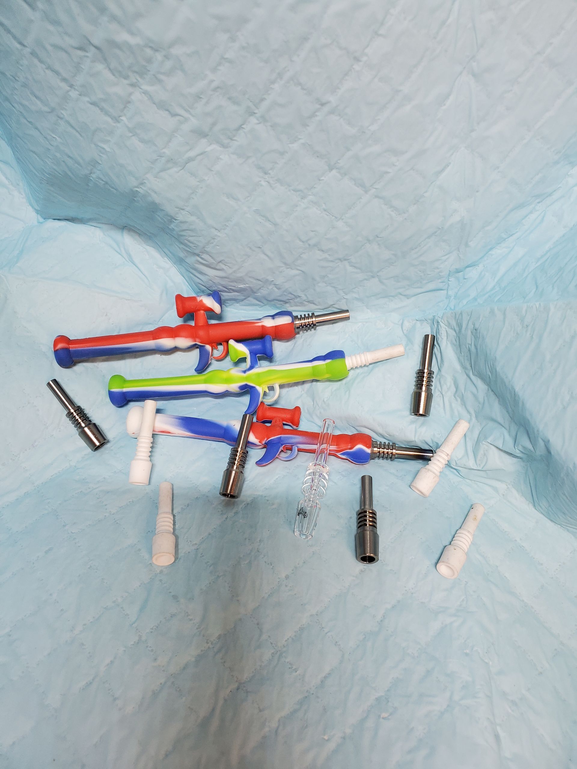 Assorted colorful toy dart guns and small accessories on a light blue quilted surface