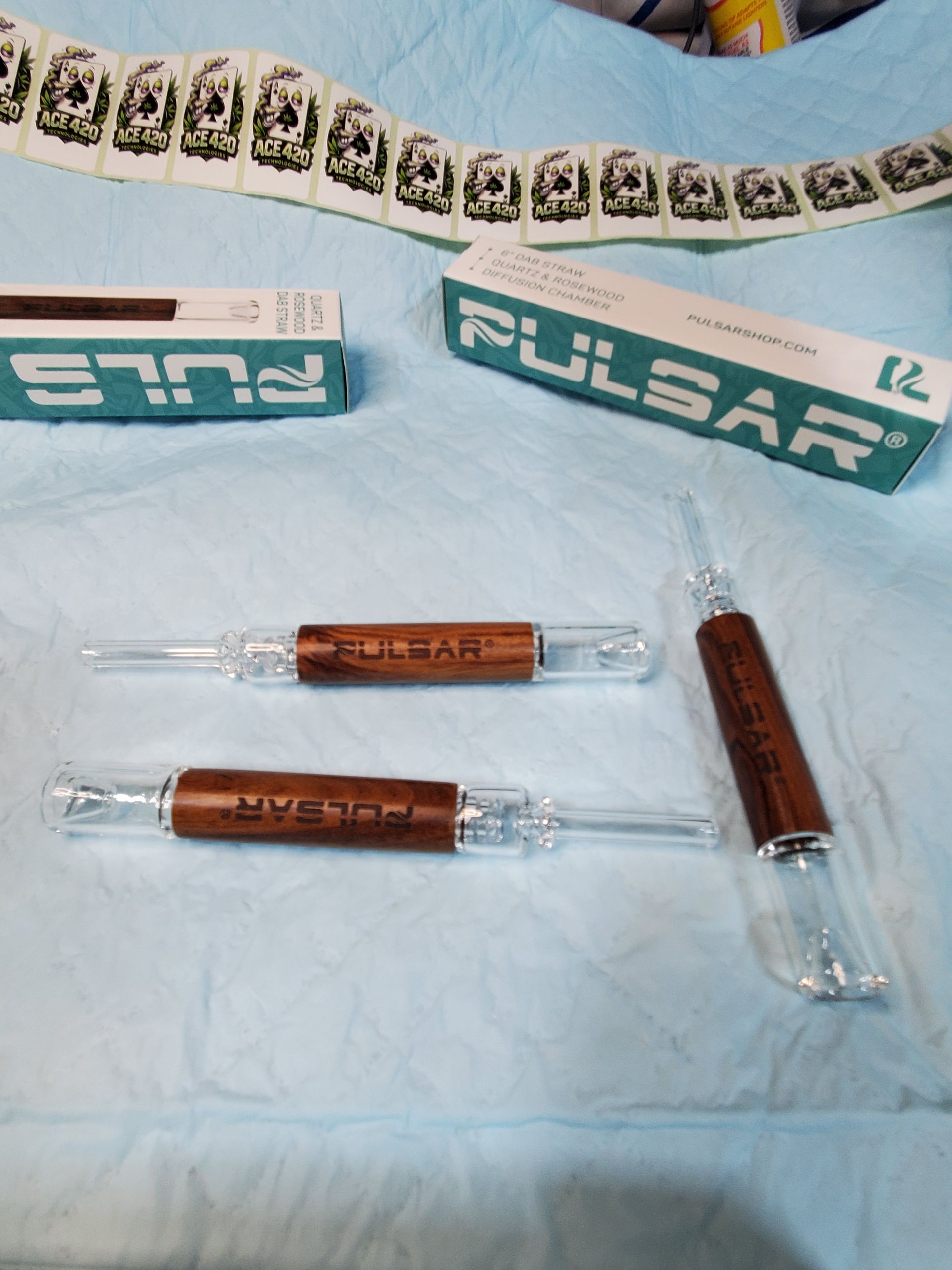 Clear glass test tubes with brown labels on a blue cloth beside PULSAR boxes.