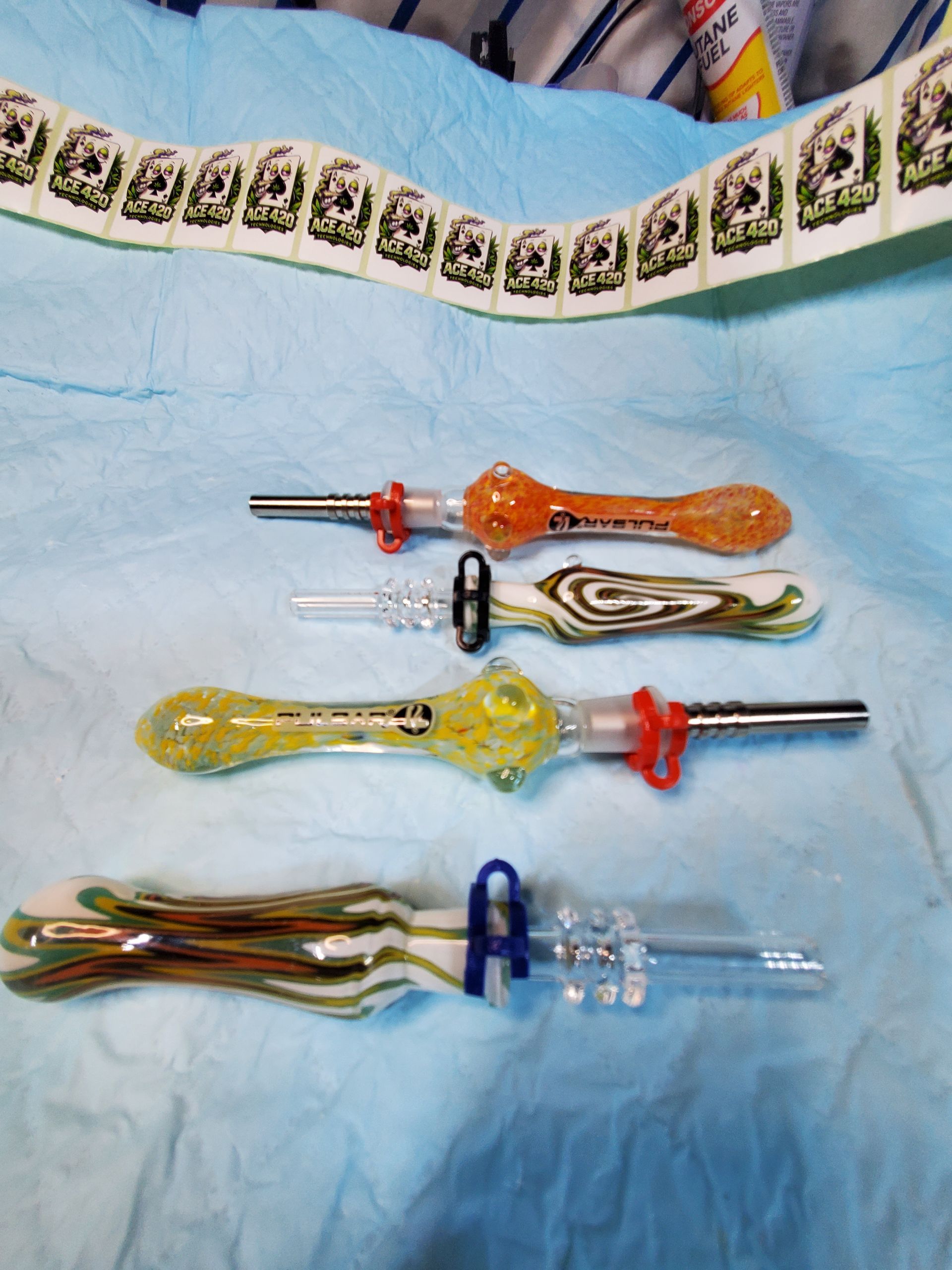 Four colorful glass dab tools on a light blue cloth, with a patterned strip at the top.
