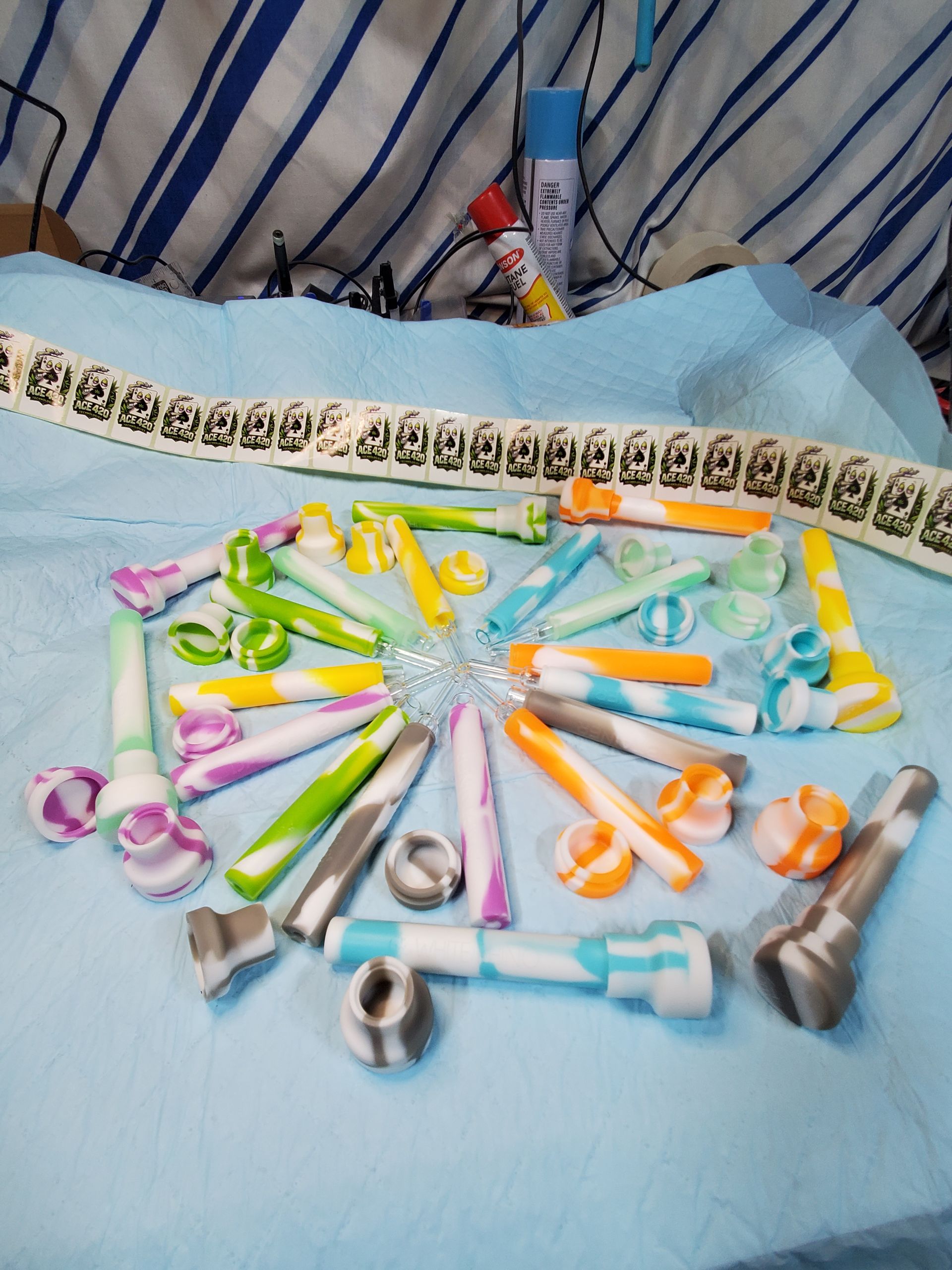 Assorted colorful razors arranged in a circle on a blue bedspread with striped pillows in the background