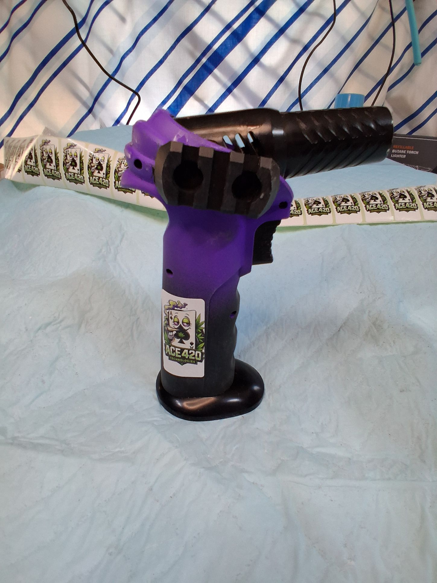 Purple-and-black handheld device with a patterned strap on a light blue bedspread