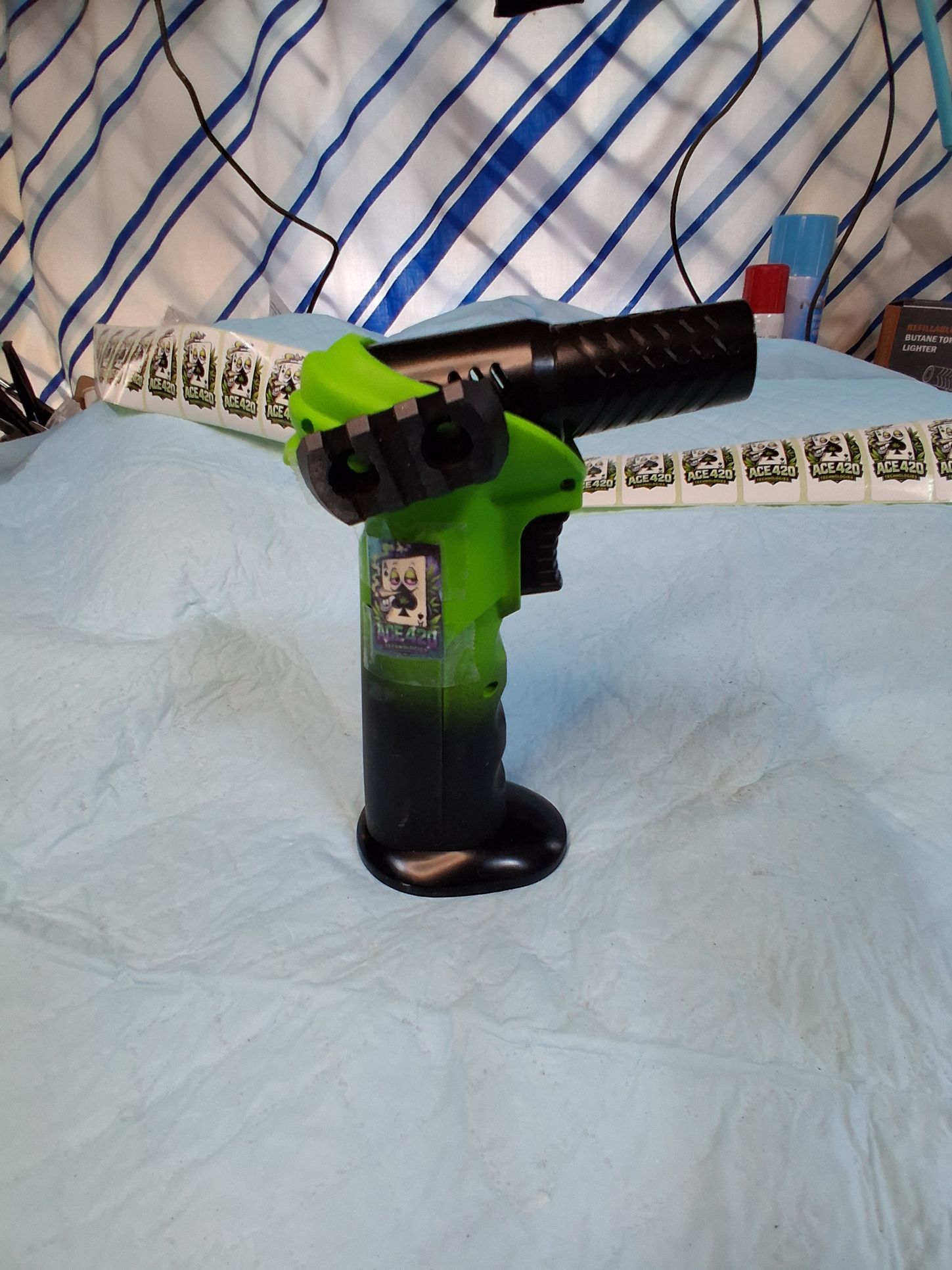 Green-and-black toy gun on a light blue bed with a patterned blanket in the background