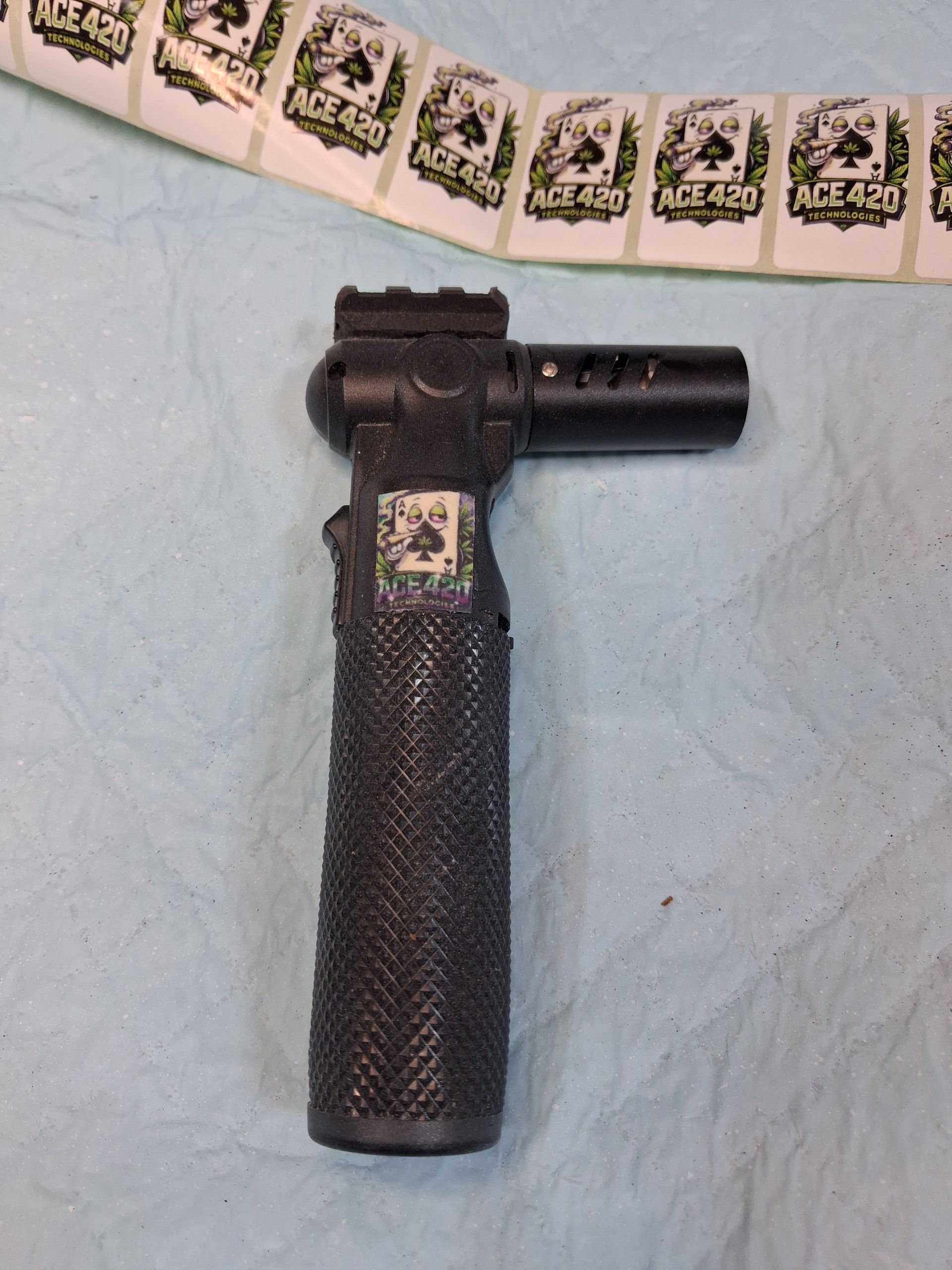 Black tactical flashlight on a light blue surface, with a strip of postage stamps above it