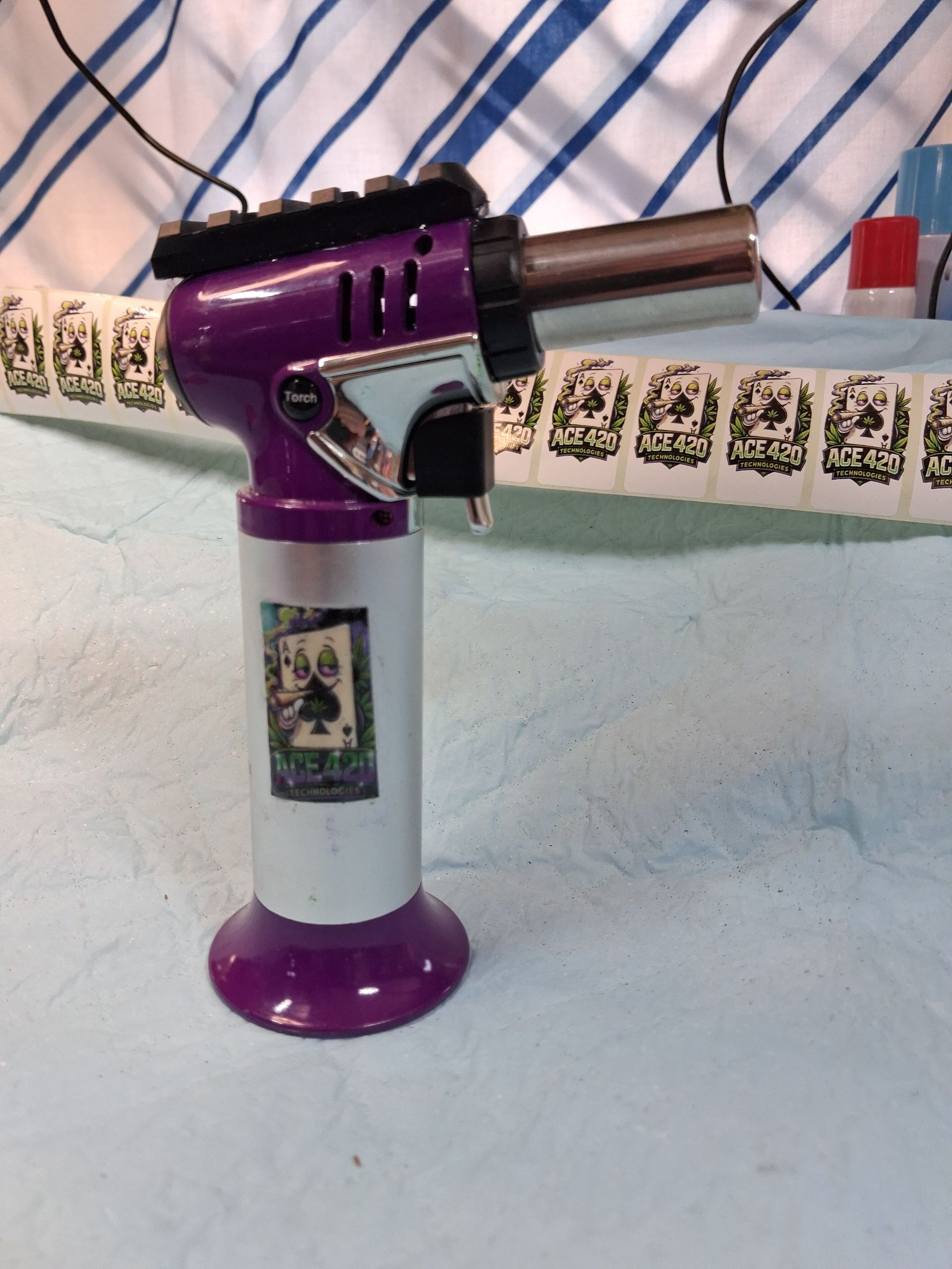 Purple and silver handheld torch lighter on a fabric surface with patterned trim