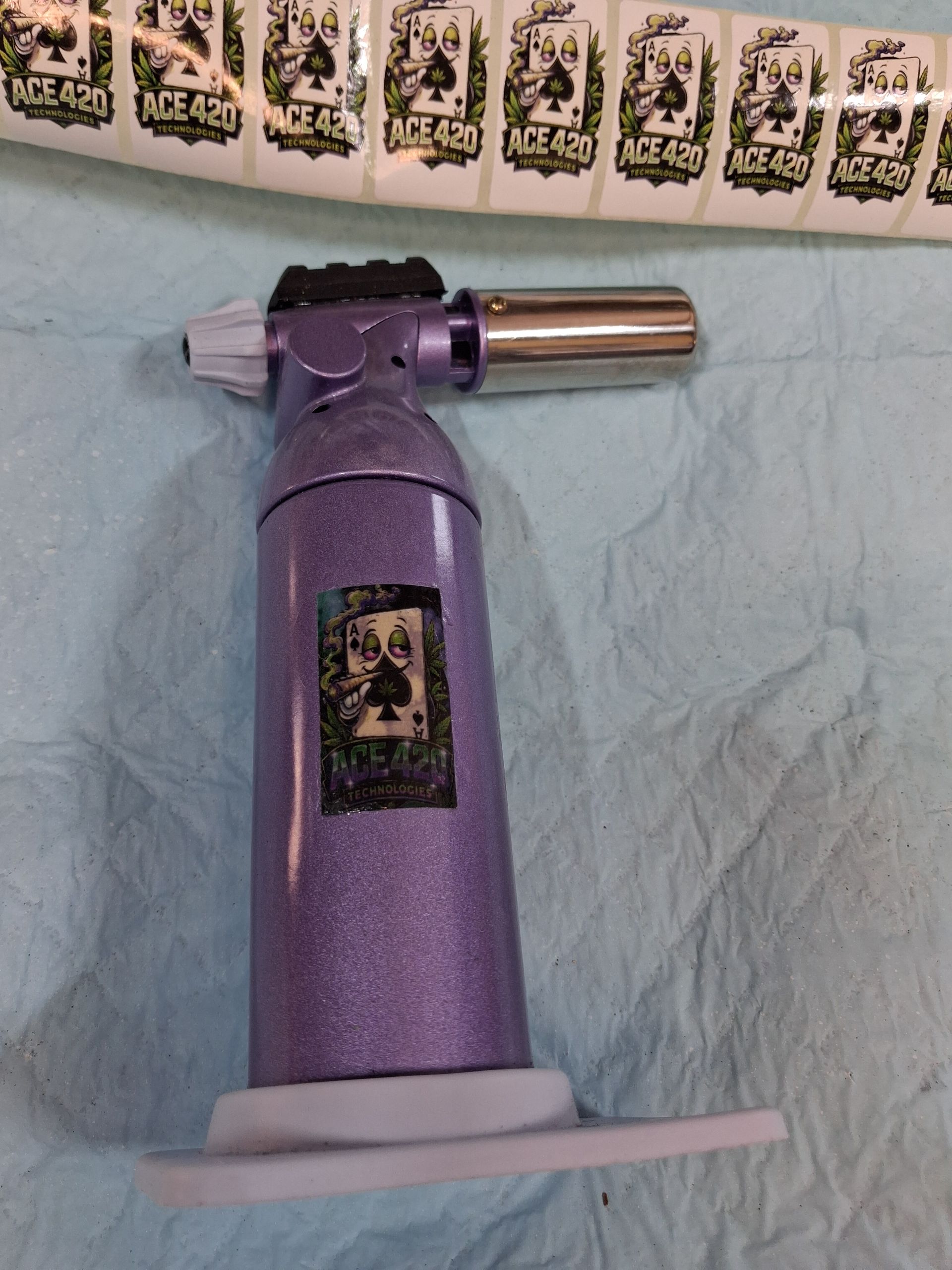 Purple lighter on a table with a silver nozzle, against a light blue wall and patterned border.