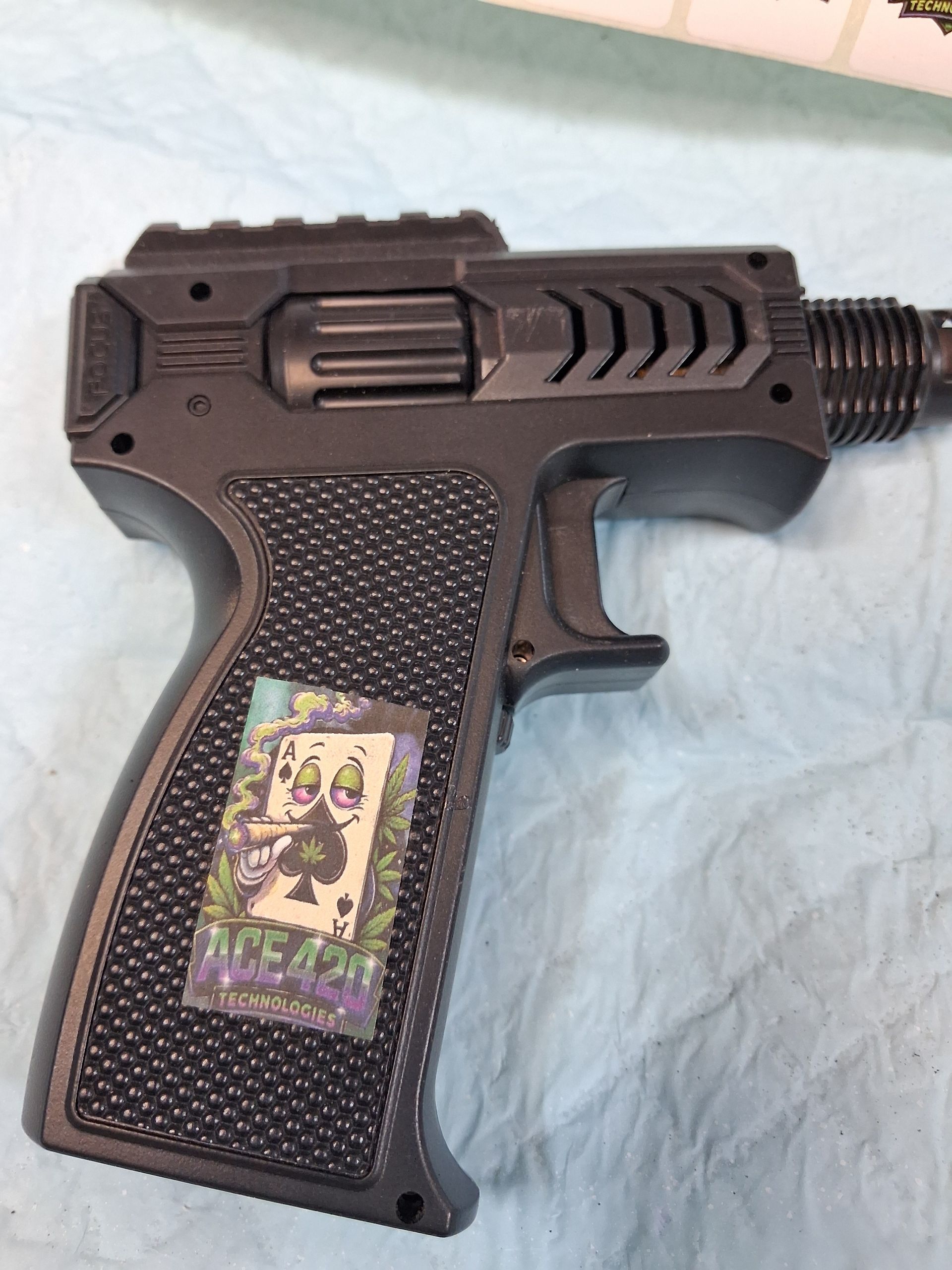 Black toy gun with textured grip and a Joker card sticker lying on a light blue surface