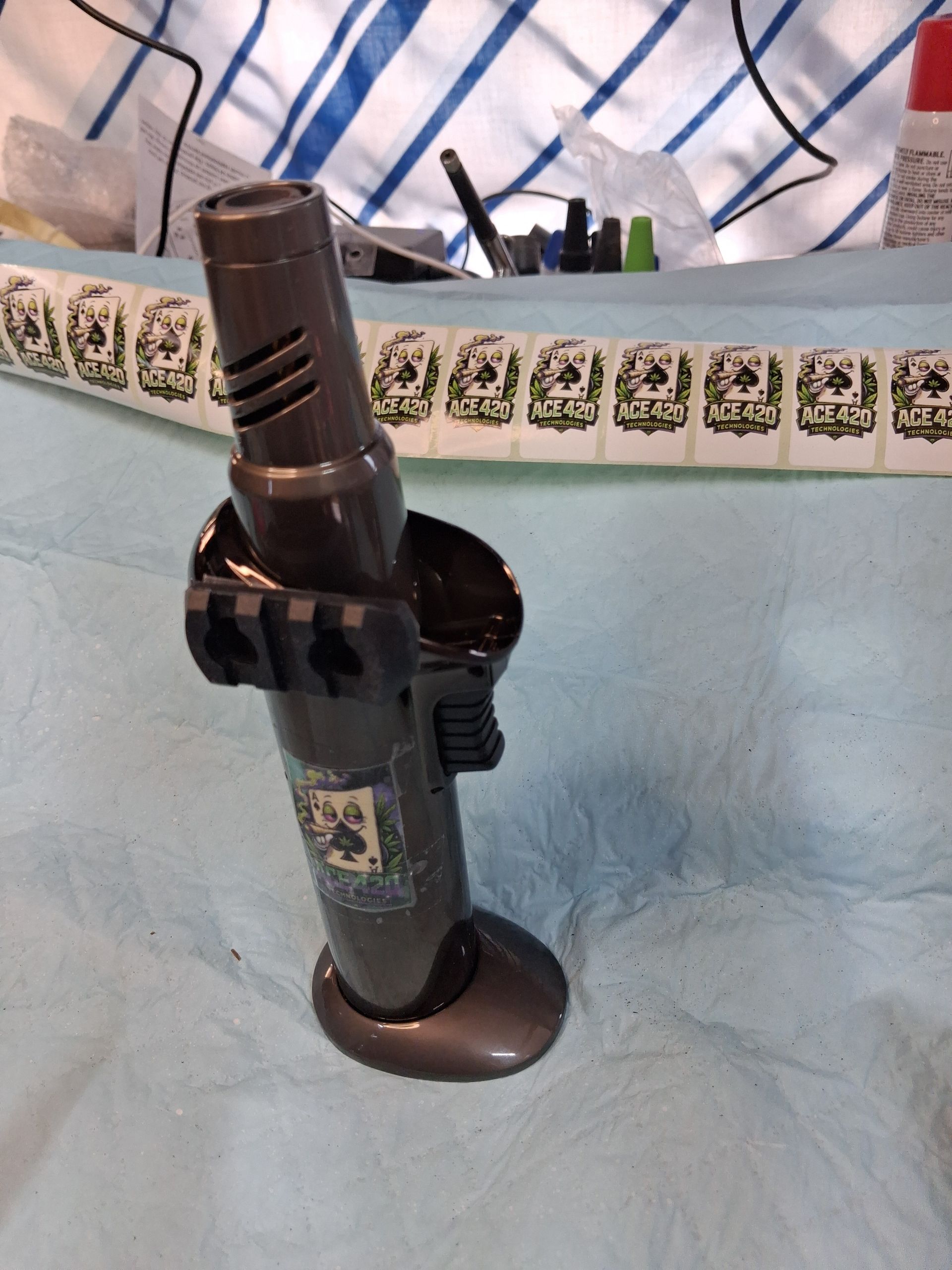 Black flashlight in a stand on a light blue tablecloth, with a patterned cloth in the background