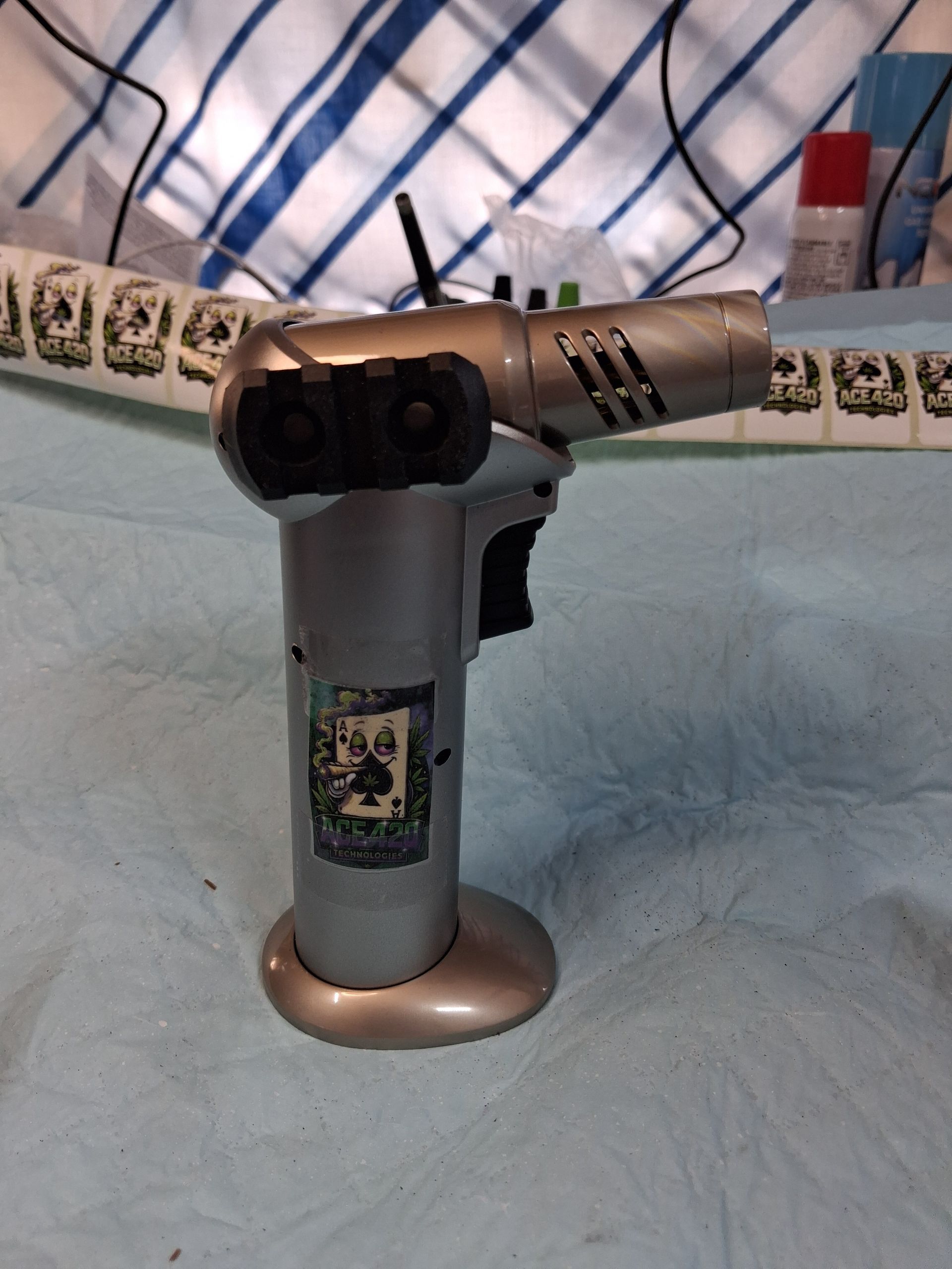 A gray toy blaster on a bed with blue-and-white striped bedding, with a red bottle in the background.