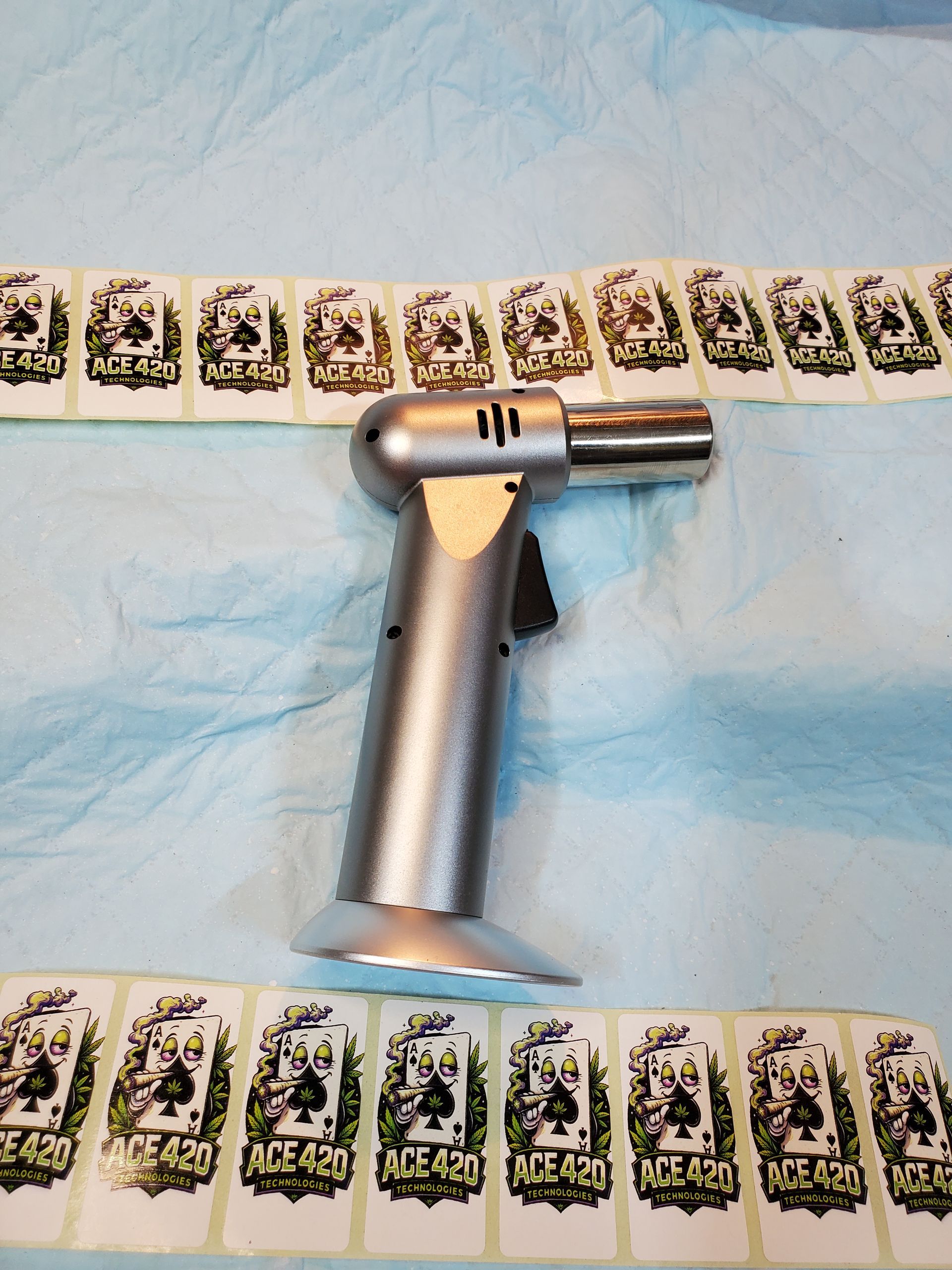 Silver metal dog training device with a suction base on a blue cloth, surrounded by a row of small patterned tiles