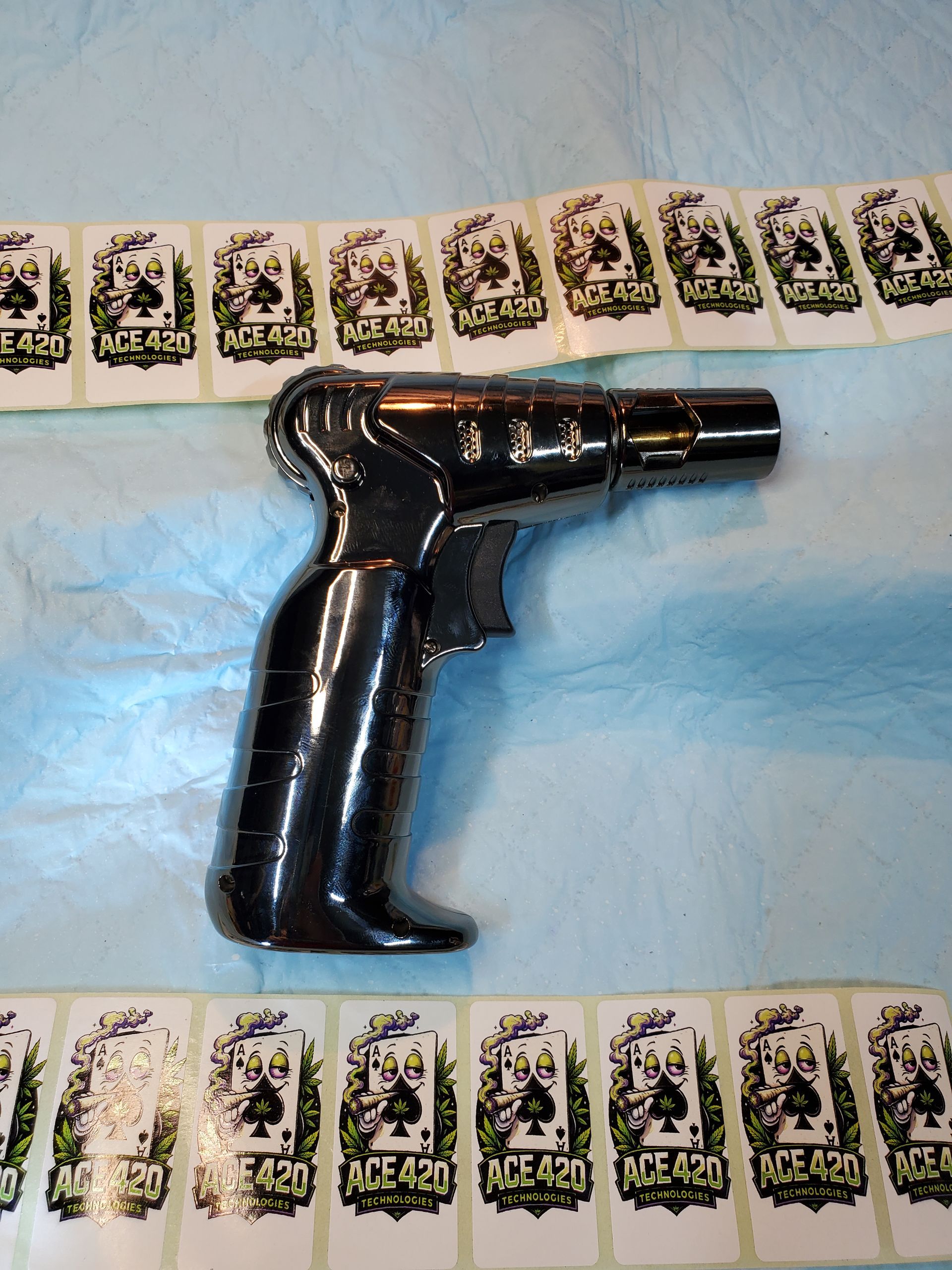Black toy pistol-shaped object on a blue cloth with patterned border strips above and below.