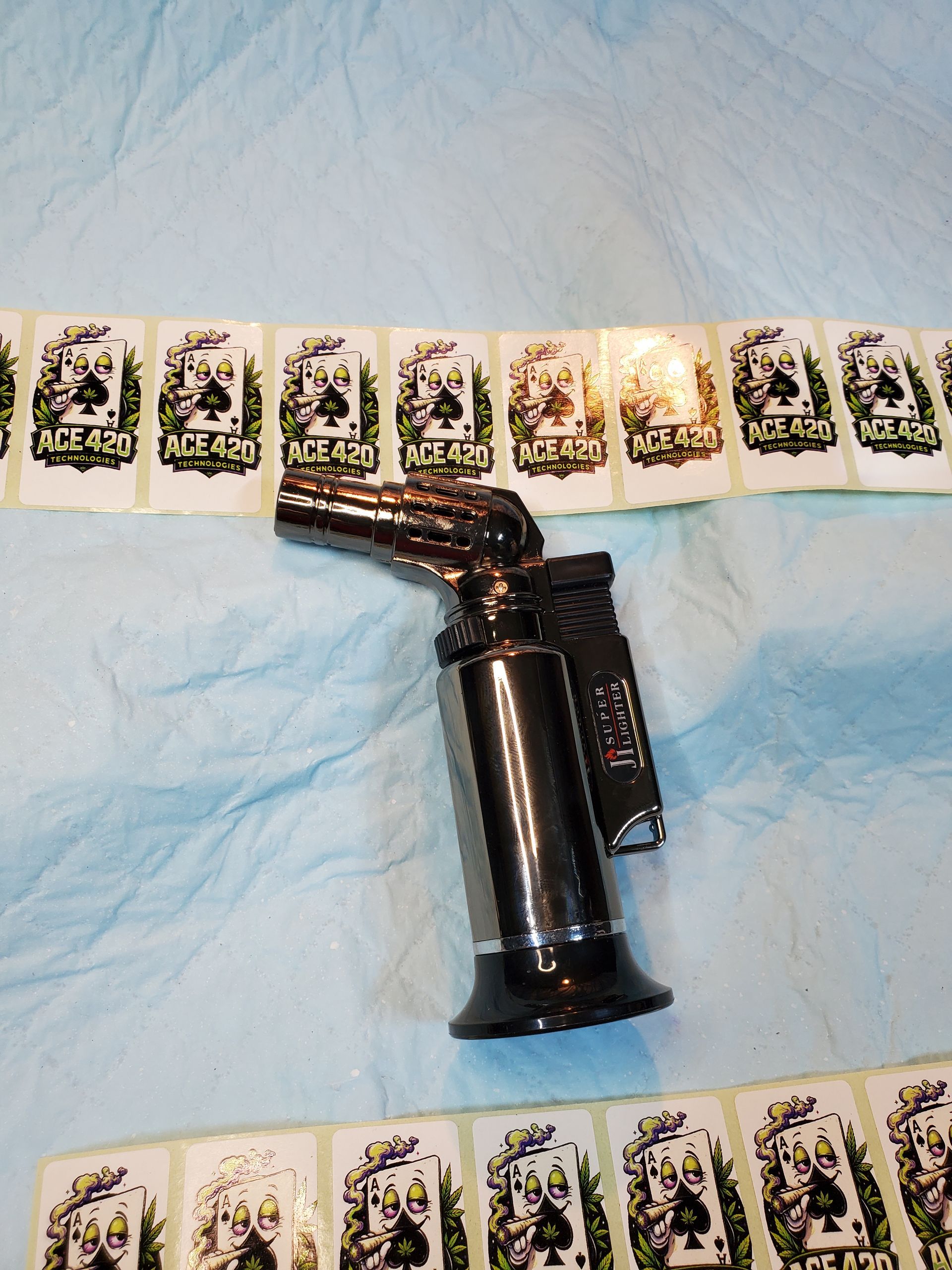 Black butane torch lighter on a blue cloth, with rows of small cards or photos in the background