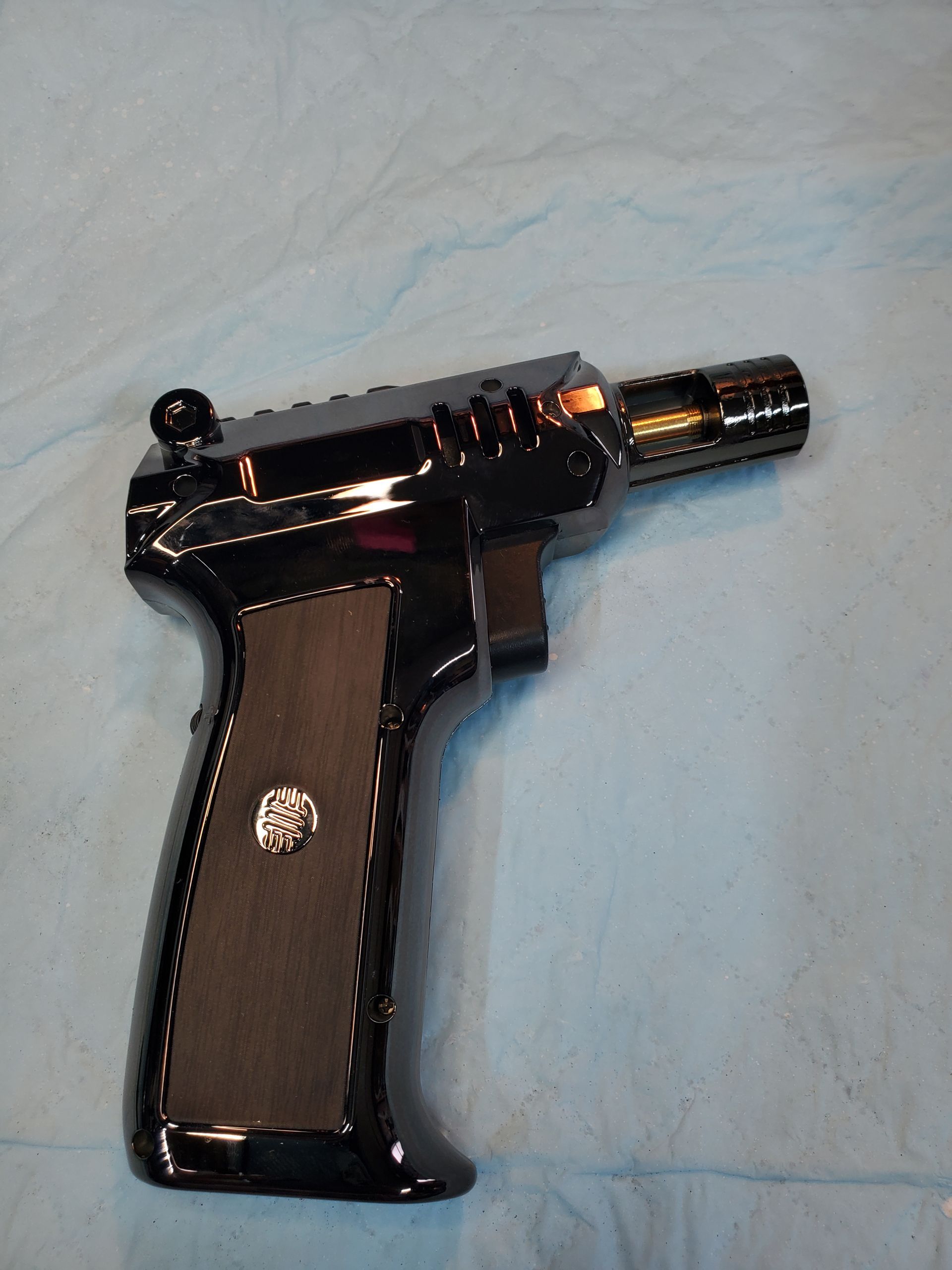 Black revolver-style toy gun with a brown grip on a light blue surface