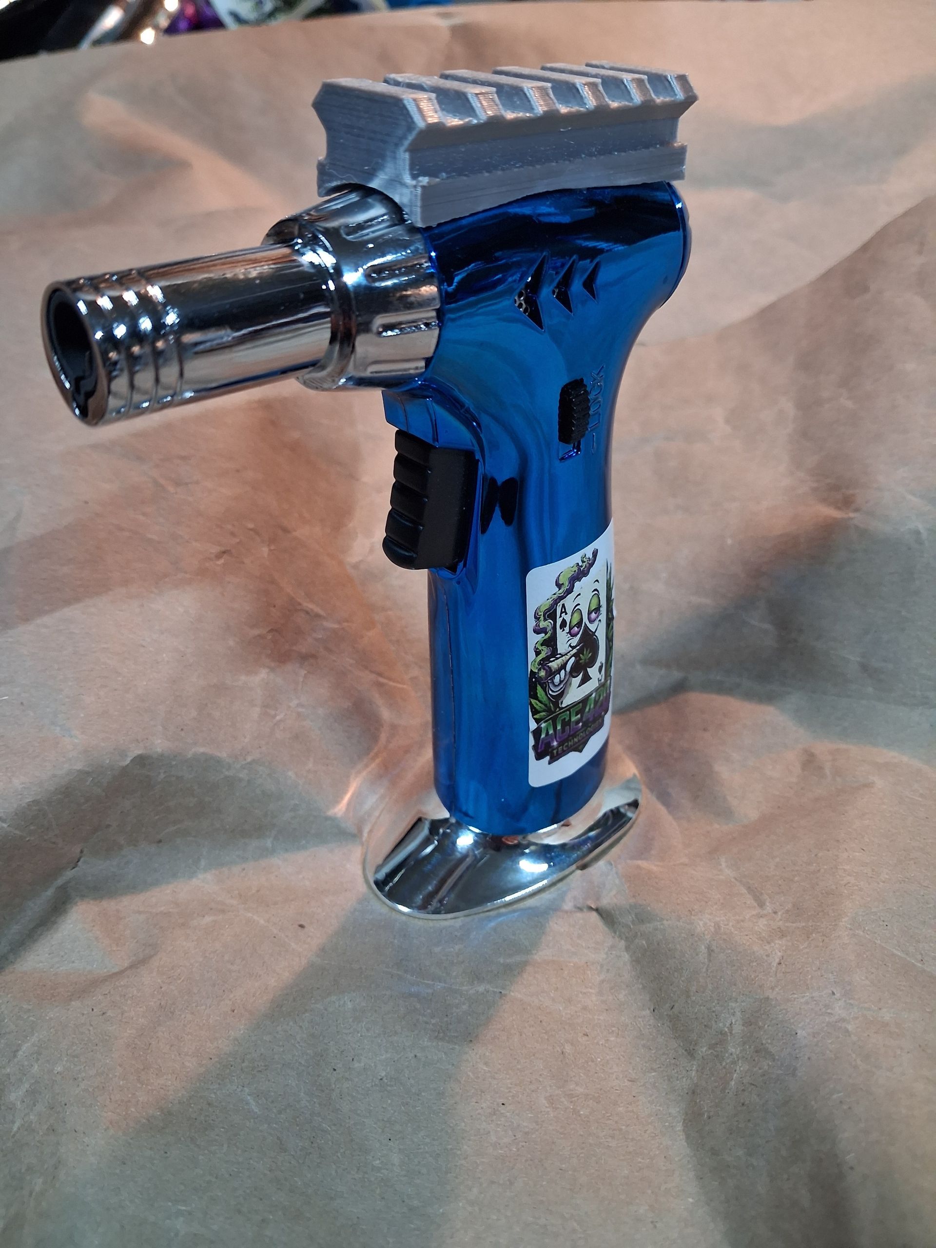 Blue handheld torch lighter with a metal nozzle and silver top on a fabric surface