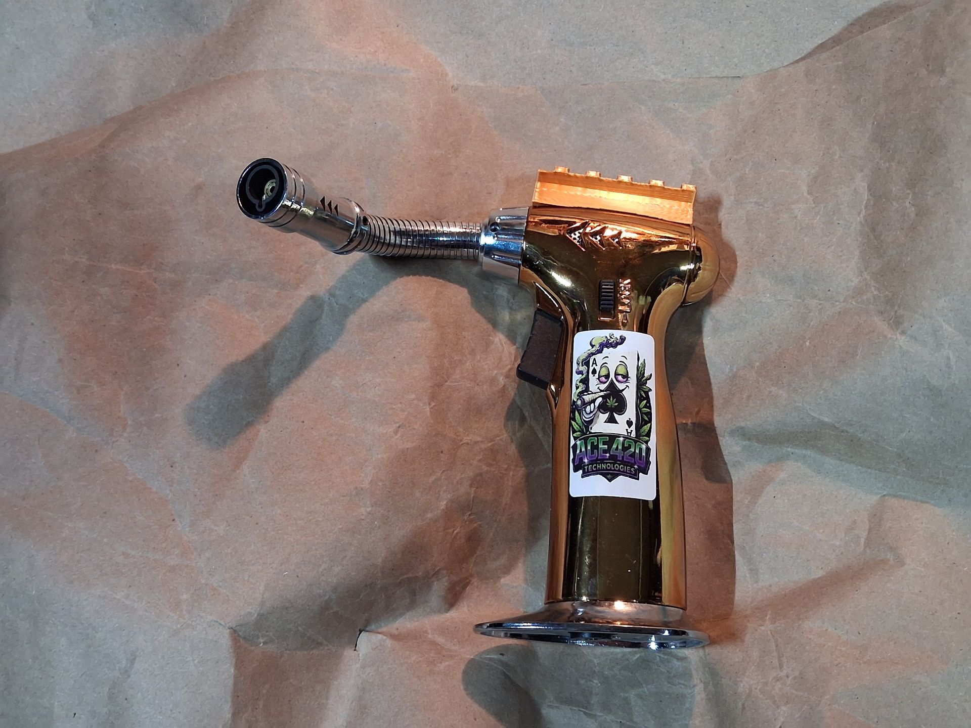 A clear glass smoking pipe with a curved mouthpiece and orange top on wrinkled paper background