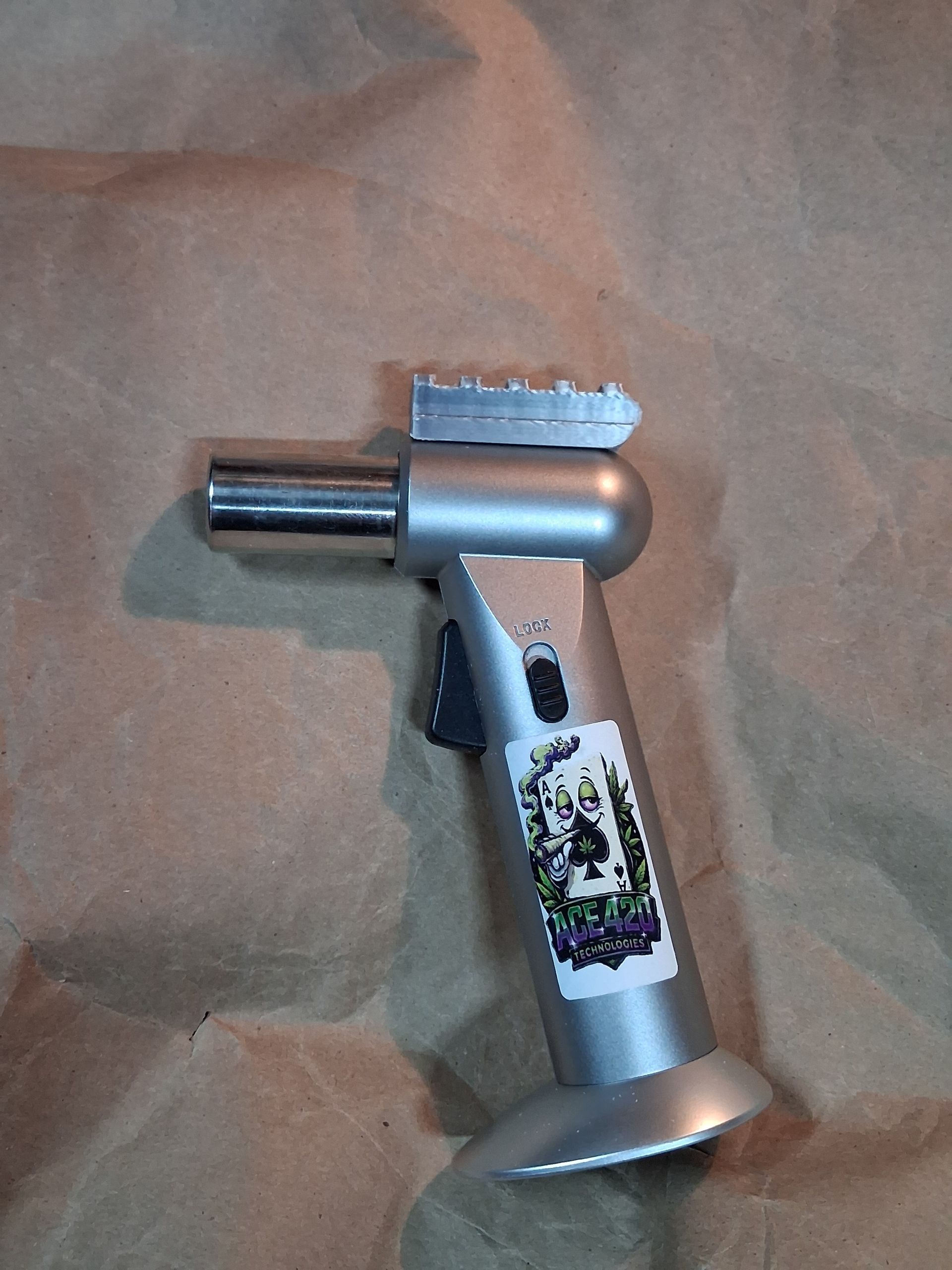 Handheld silver tool with a cylindrical nozzle and flat, textured tip, resting on brown fabric.