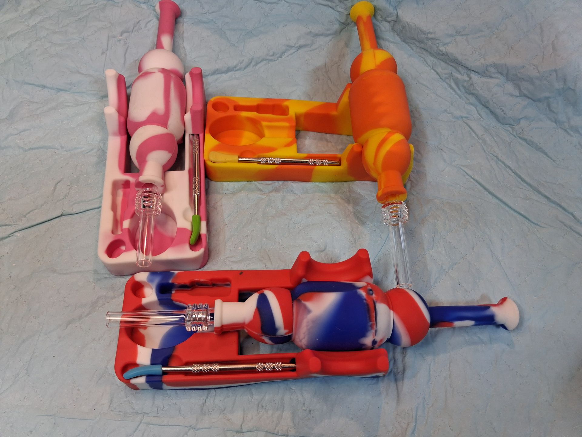 Three toy figure figures in pink, orange, and blue boxes lying on a gray crumpled fabric background
