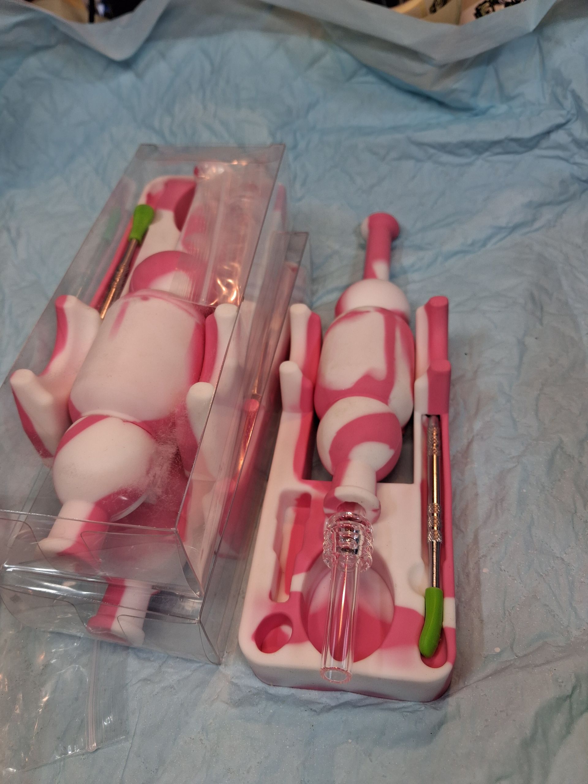 Two pink-and-white plush toys in clear plastic packaging on a blue bedspread.