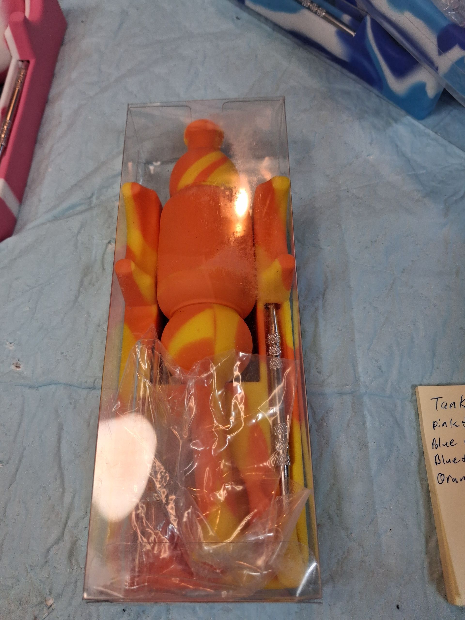 Orange toy in a clear plastic box on a blue surface, with other items partially visible nearby.