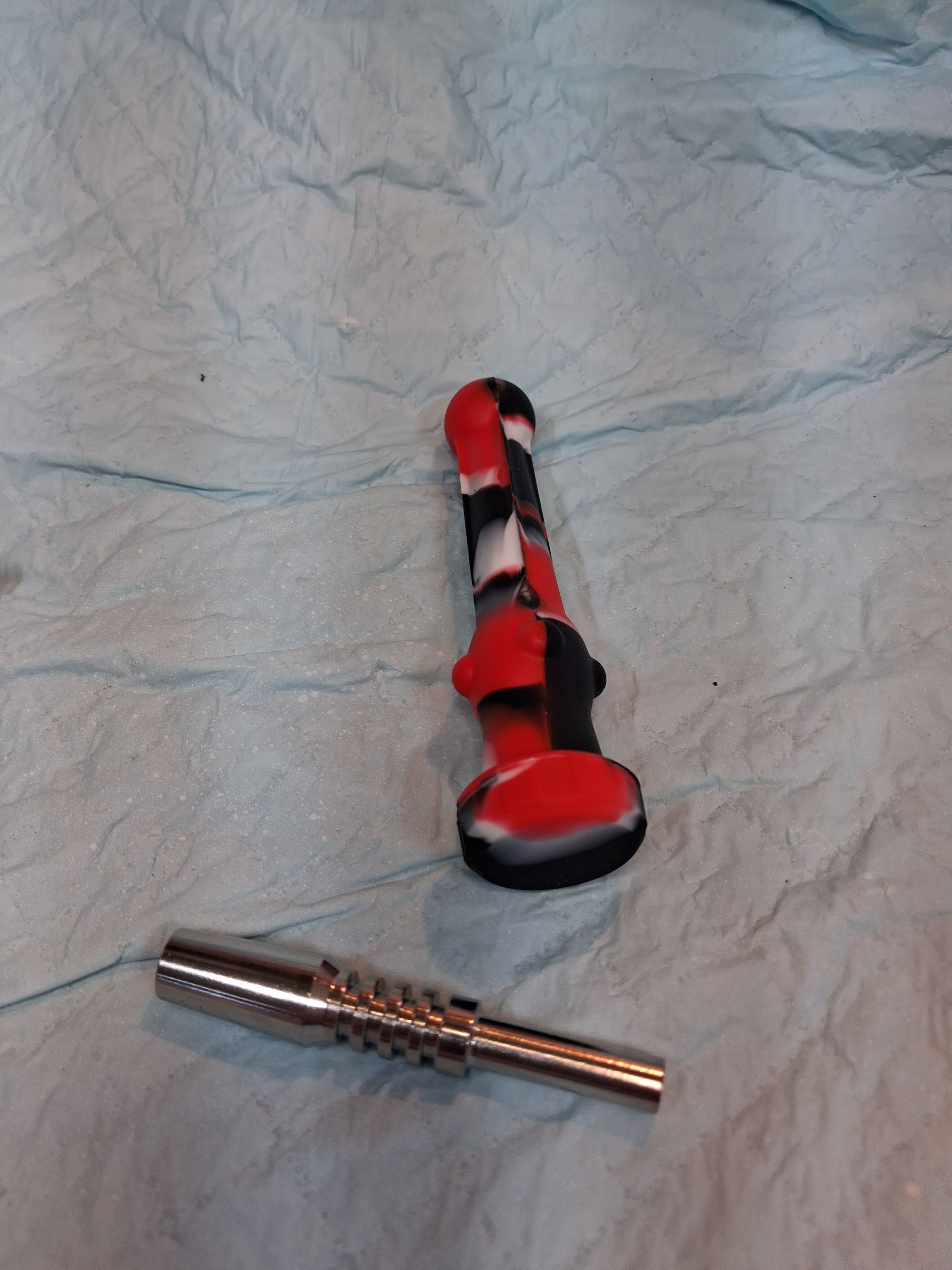 Red-and-black object and a small silver tool lying on a crumpled light blue surface.