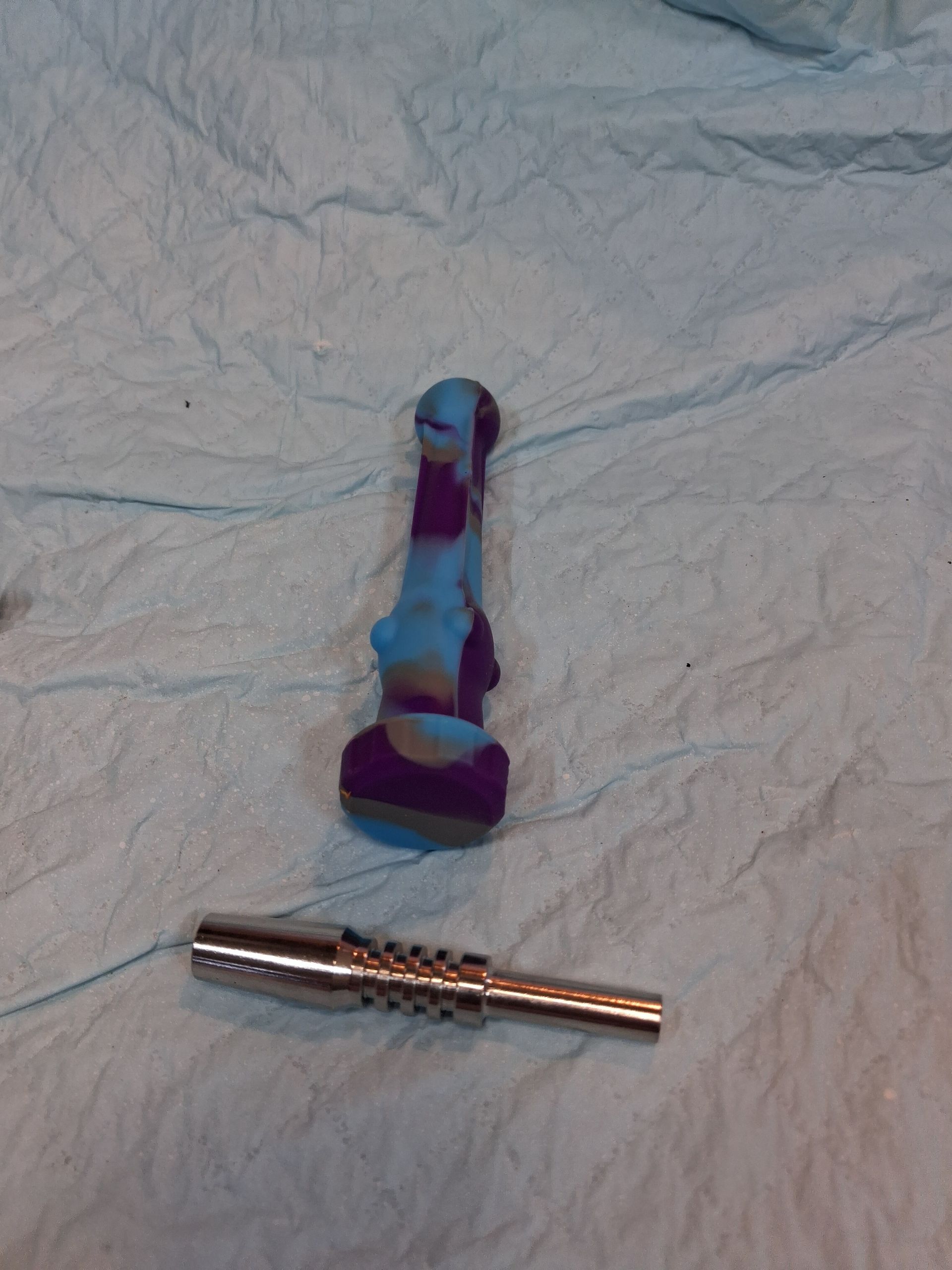 A small purple-blue sex toy and a metallic cylindrical piece on a wrinkled white cloth.