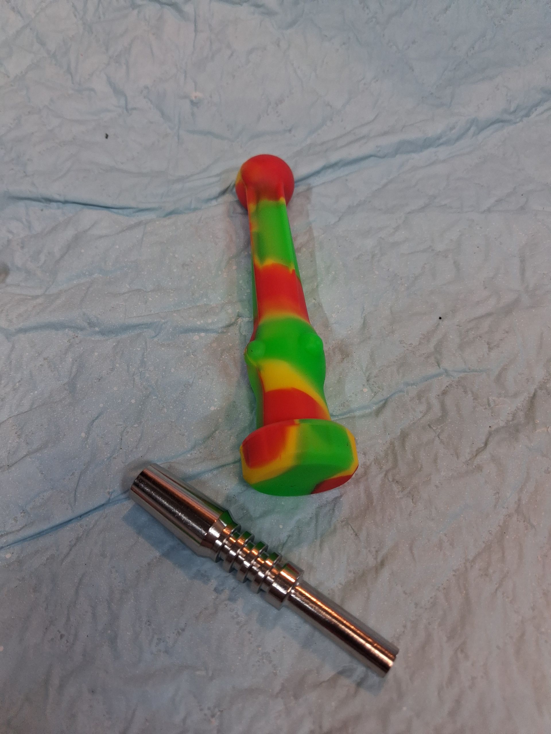 Red, green, and orange toy on a light blue surface next to a small silver metal tool