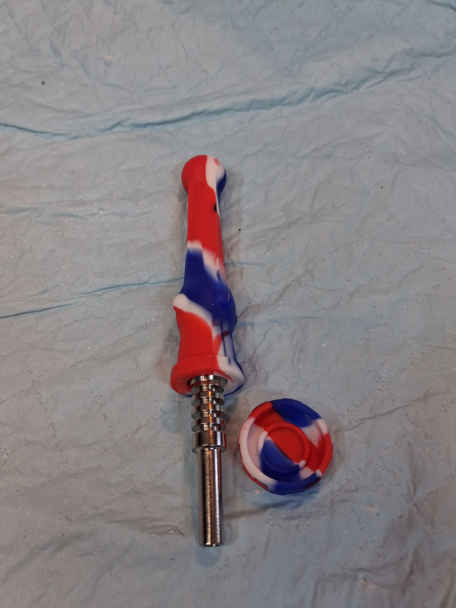 Red, white, and blue swirled dental handpiece with a matching small circular accessory on a light fabric background