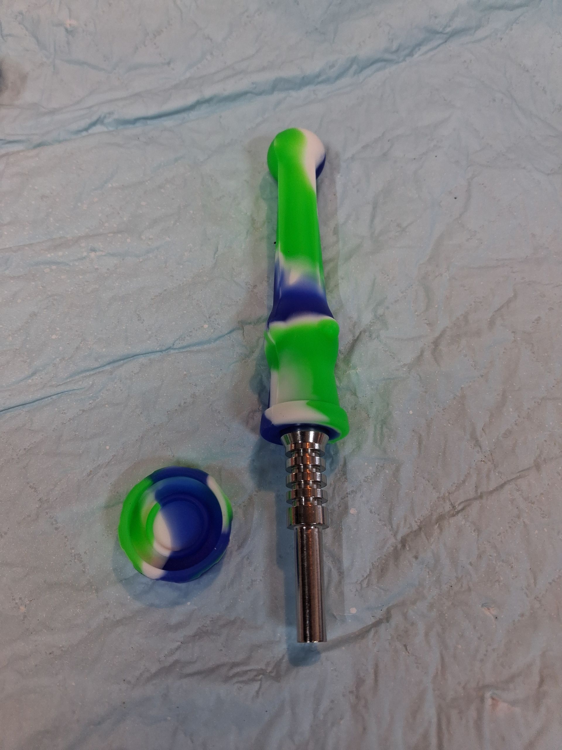 Small green-and-blue plastic tool with a metal shaft, beside a matching blue ring on a light surface