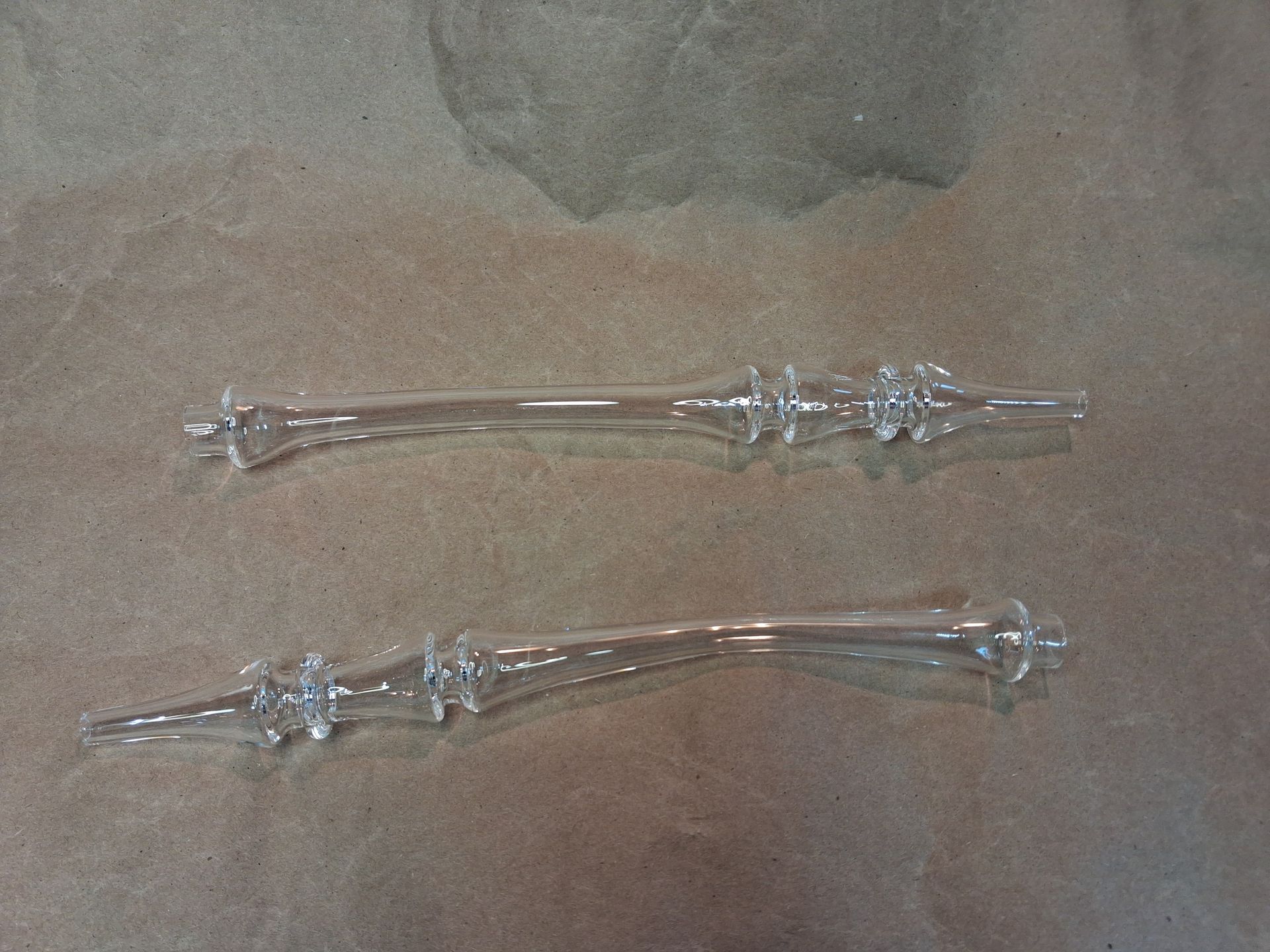 Two clear glass candle holders with decorative stems on a beige surface