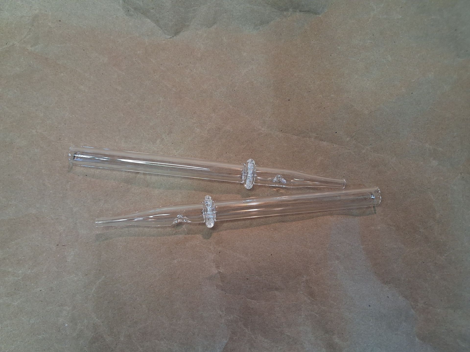 Two clear glass straws arranged on a brown paper.