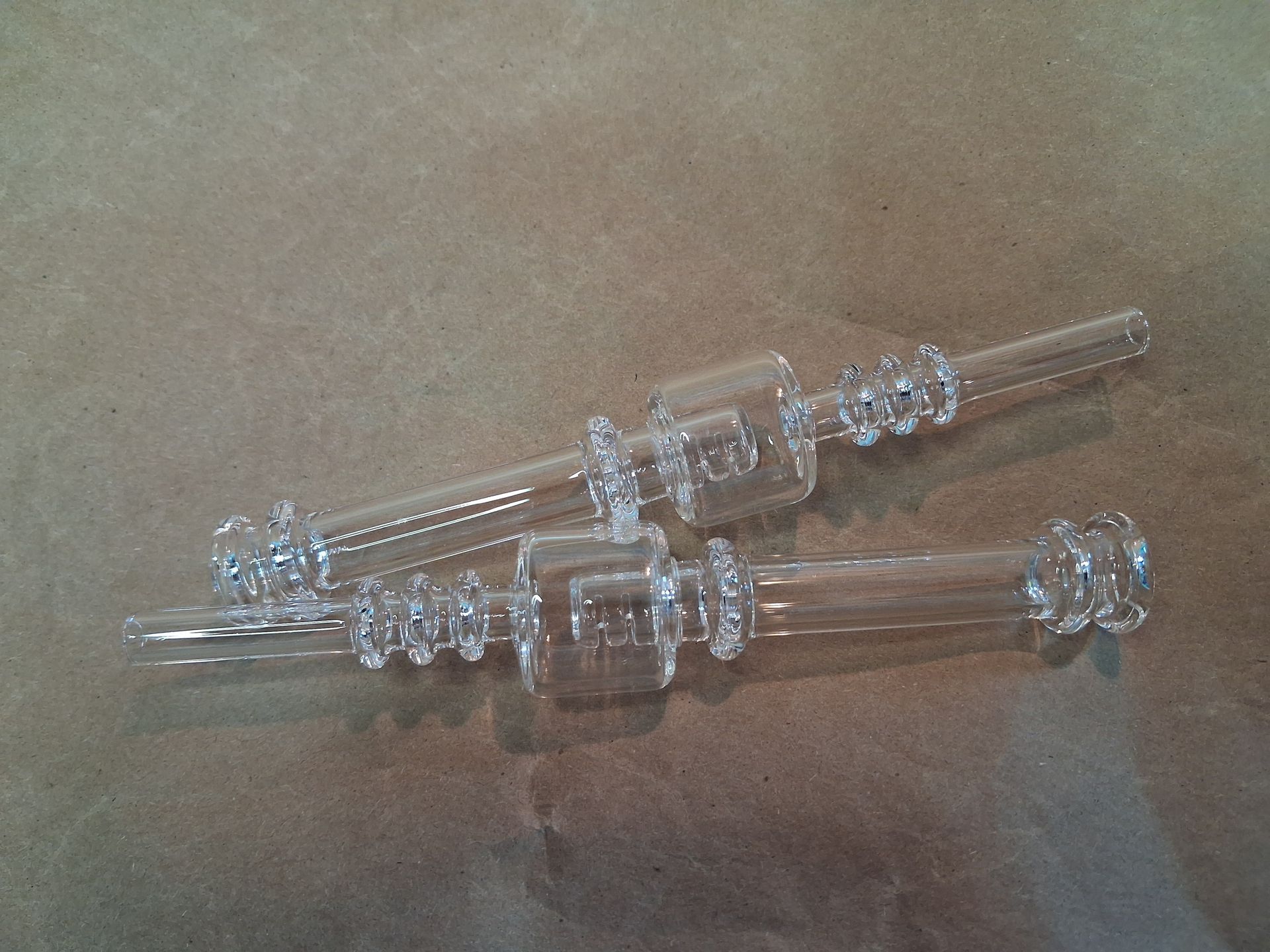 Two clear glass straws arranged on a brown paper.