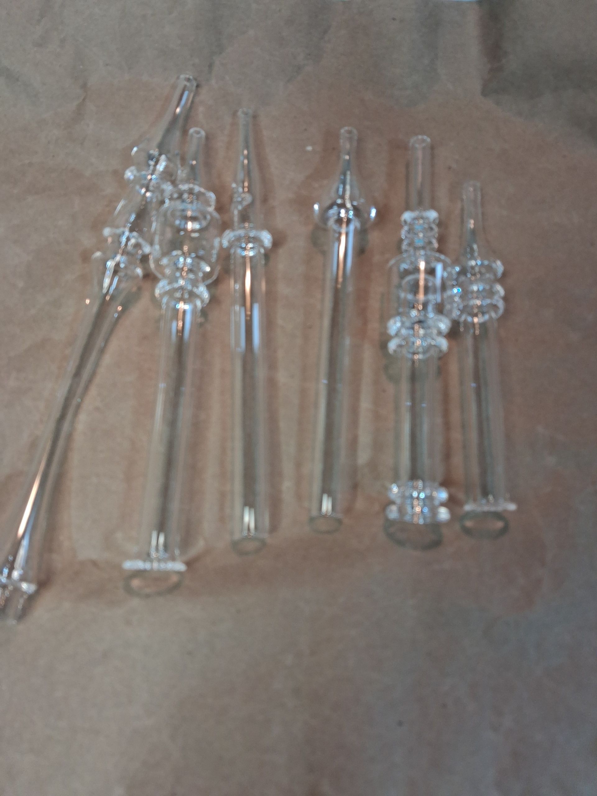 Assorted clear glass straws arranged on a brown paper.