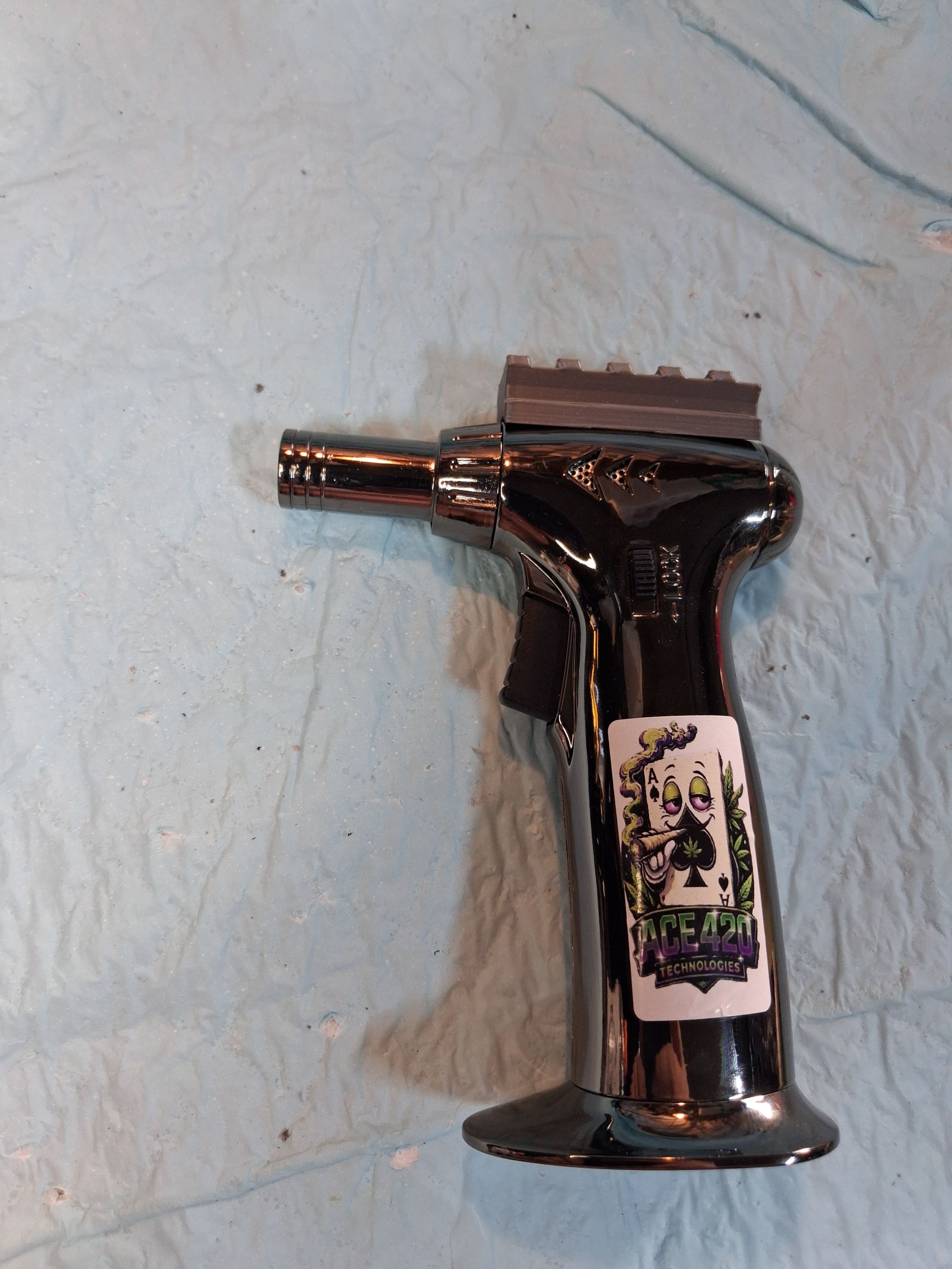 Black handheld tool with a nozzle and label resting on a light blue cloth.