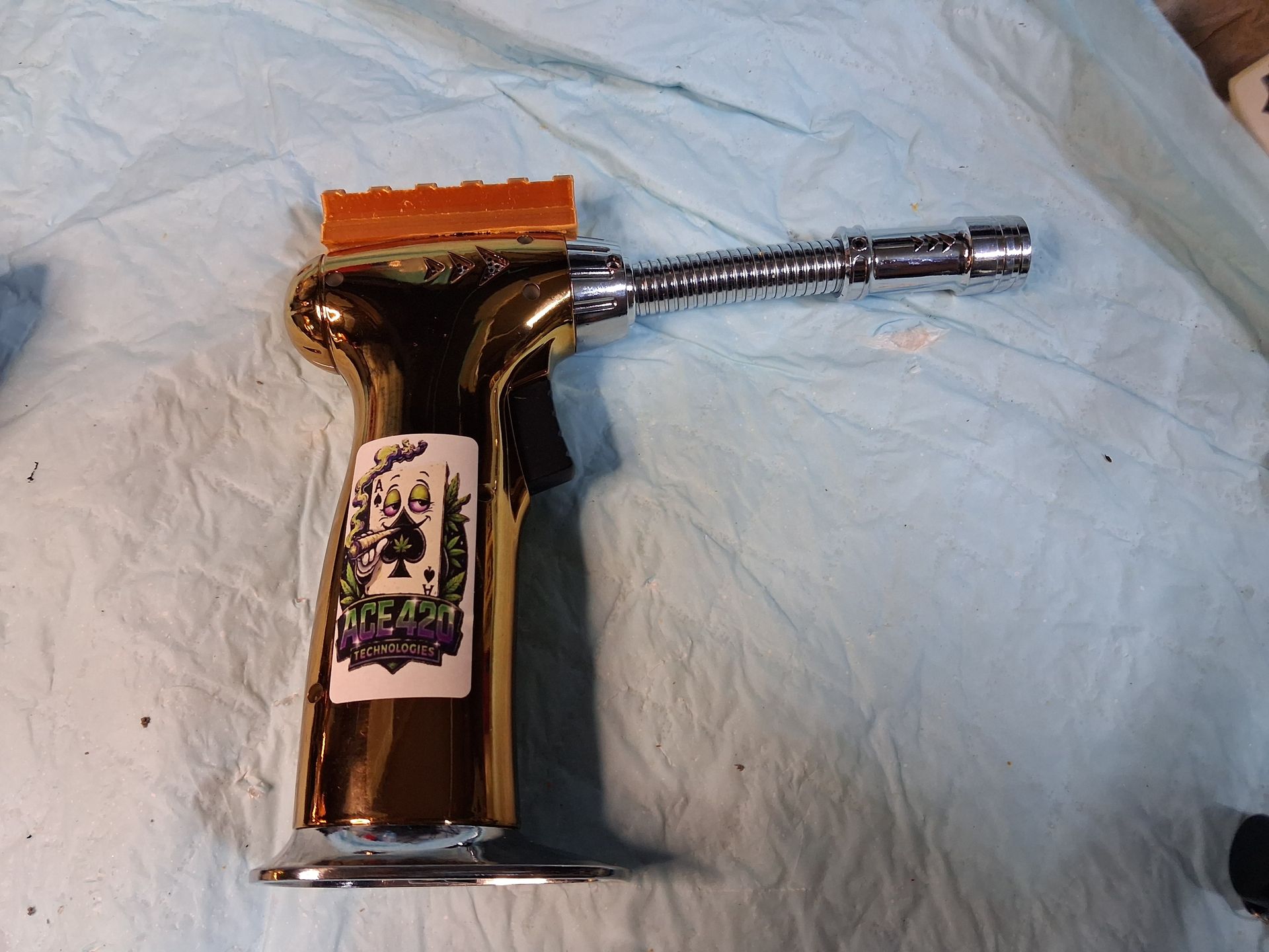 Gold metal torch lighter with long flexible nozzle lying on a light blue cloth