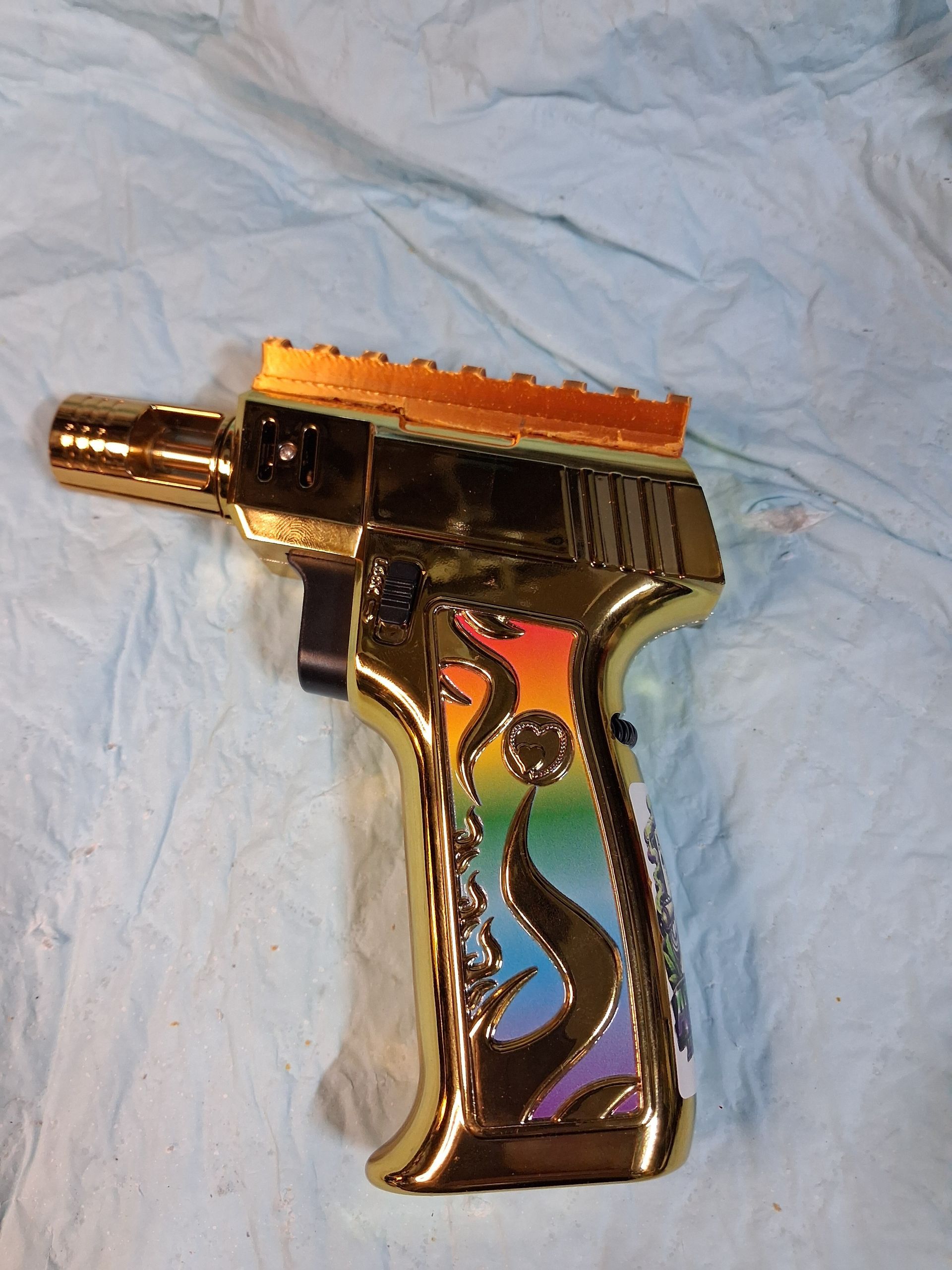 Gold toy gun with colorful flame design on a light blue cloth background