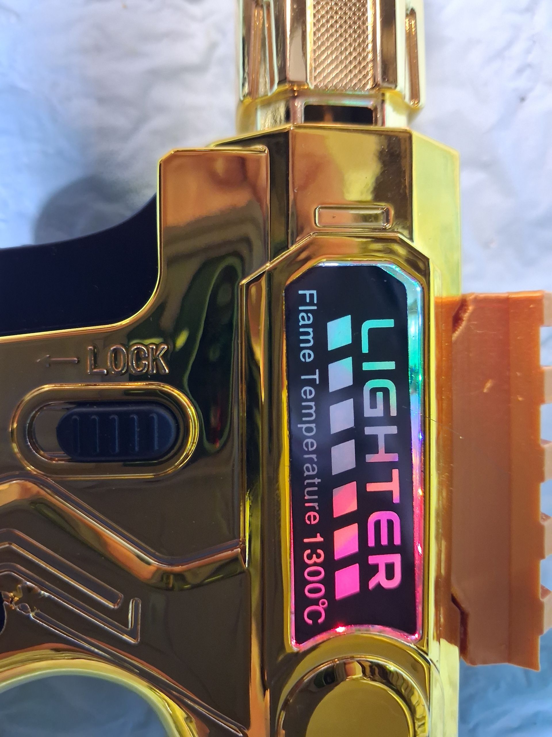 Close-up of a gold butane torch with a glowing display reading “Vuse Vighter” and “1300C.”