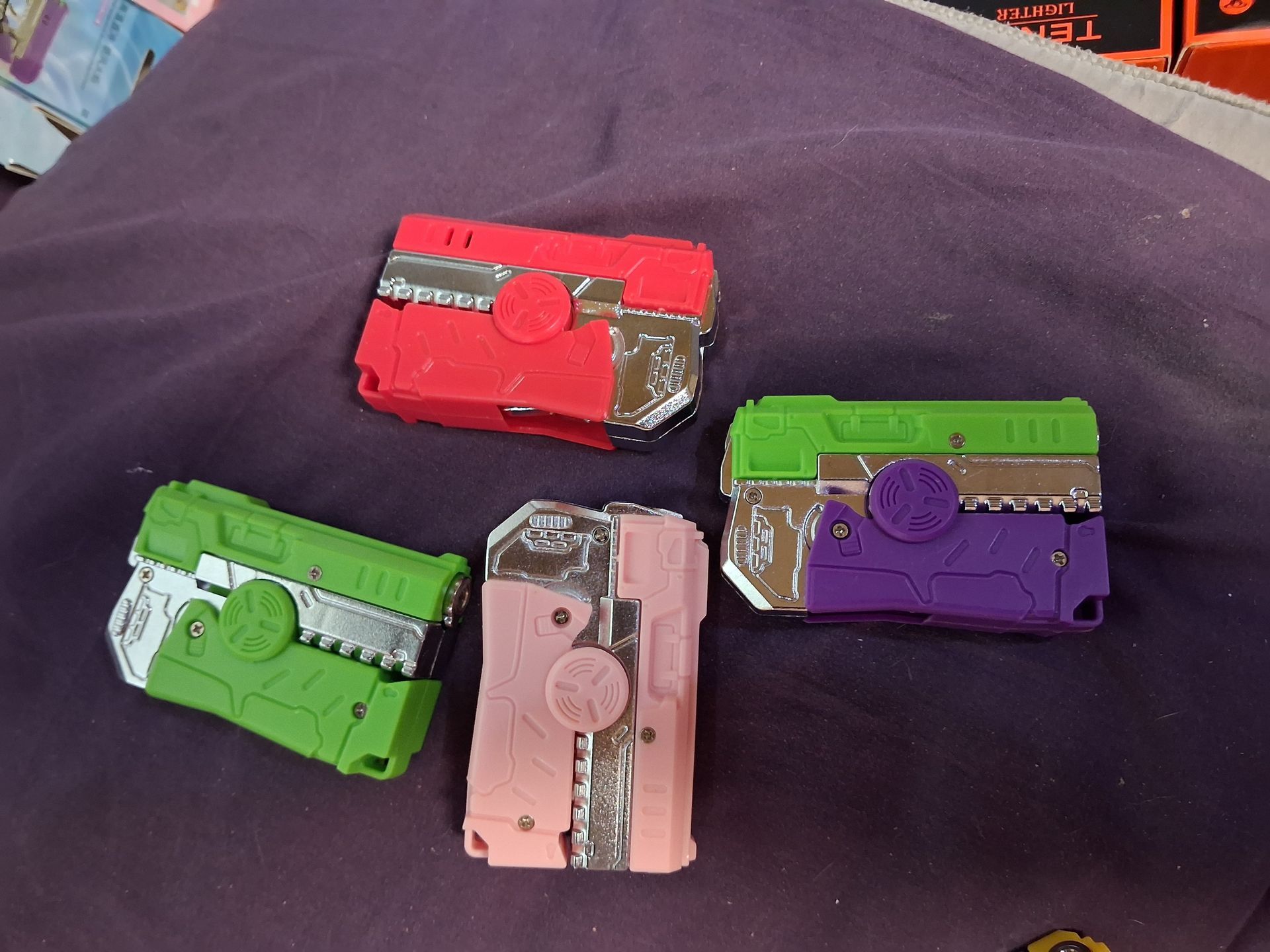 Four colorful toy blaster-like devices arranged on a dark fabric surface.