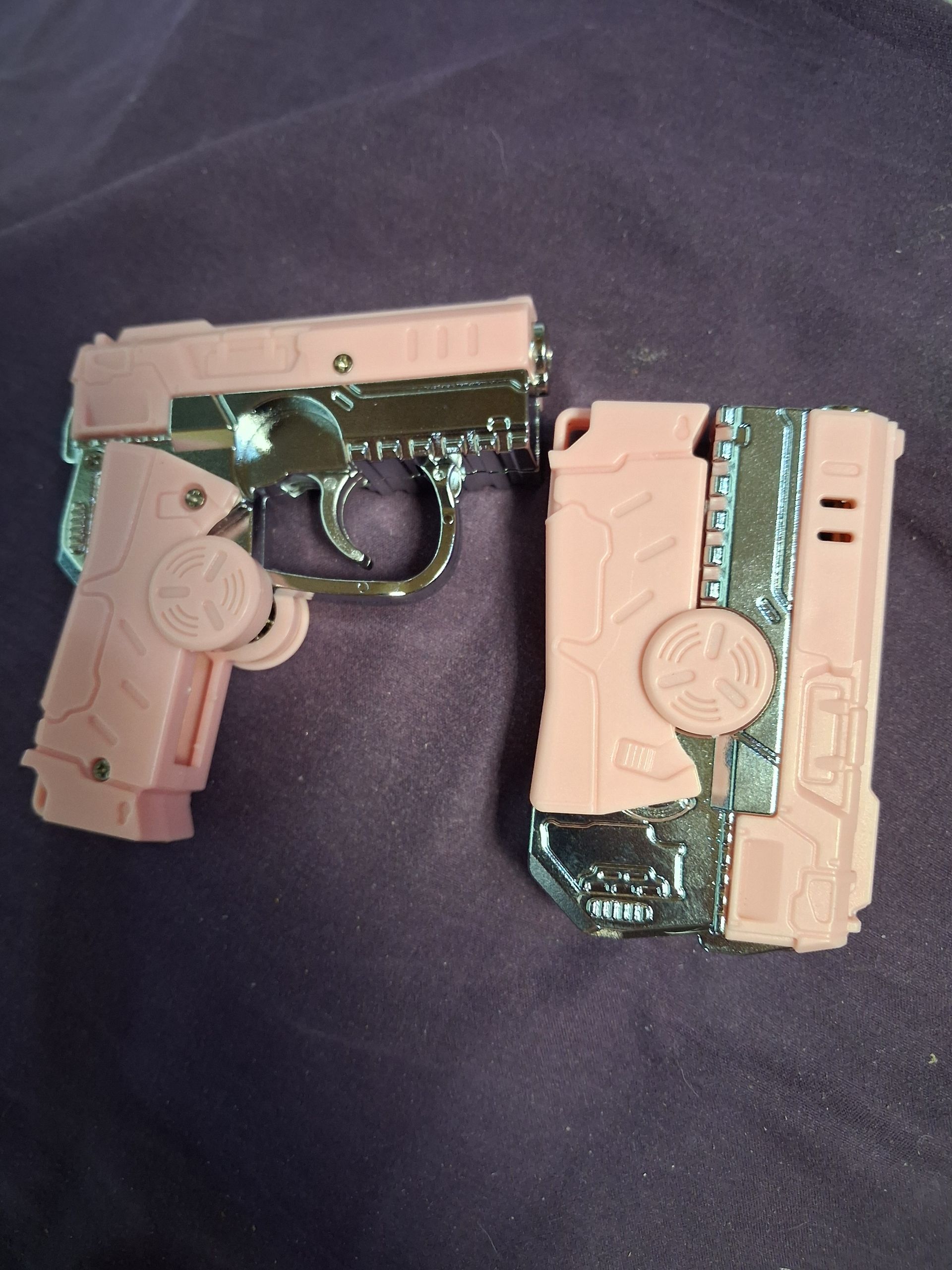 Two small tan-and-black toy gun parts lying on dark fabric.