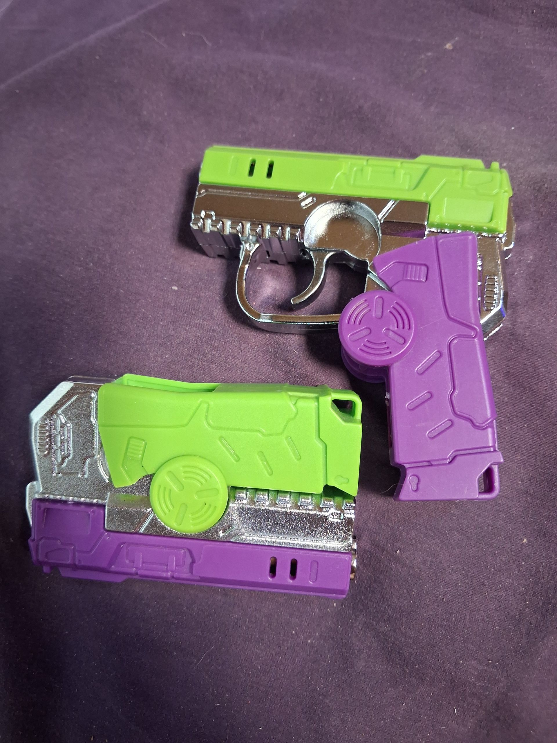 Three small neon green and purple toy pistols on a dark fabric surface